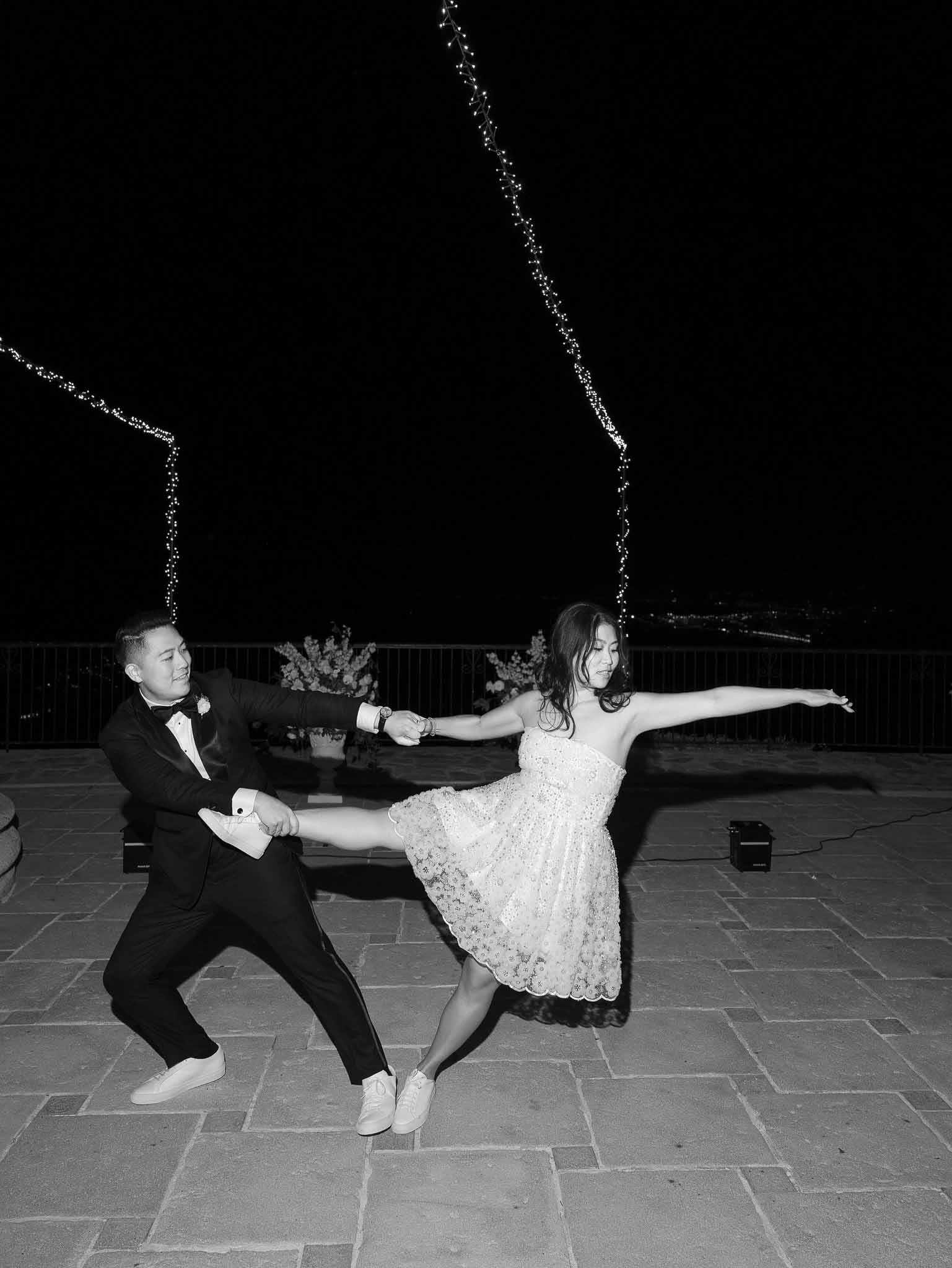 Couple dancing on outdoor terrace during wedding reception at night with string lights