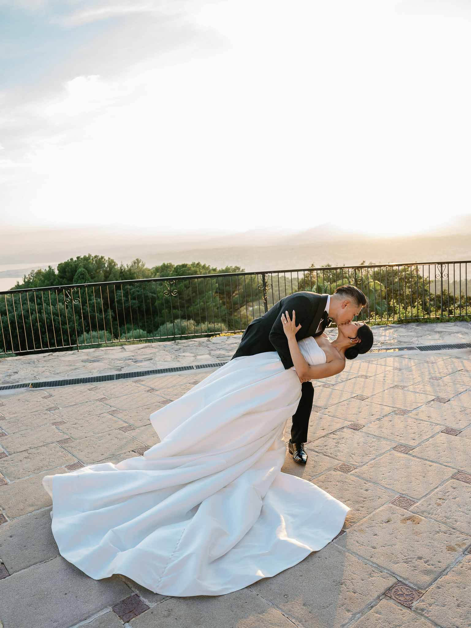 Groom dips bride in dramatic pose on stone terrace with panoramic mountain views