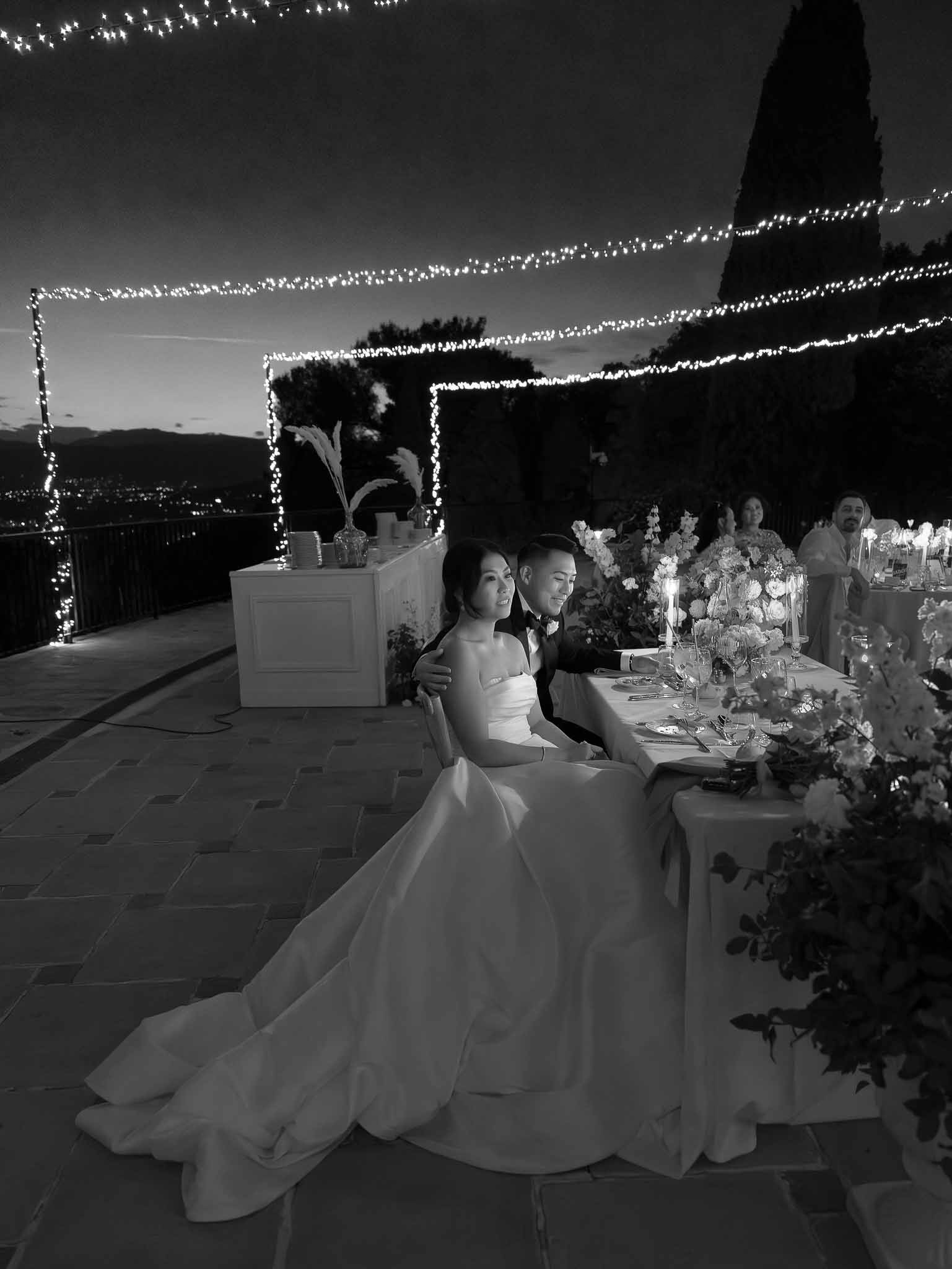 Black and white reception dinner at outdoor hilltop venue with string lights and landscape views