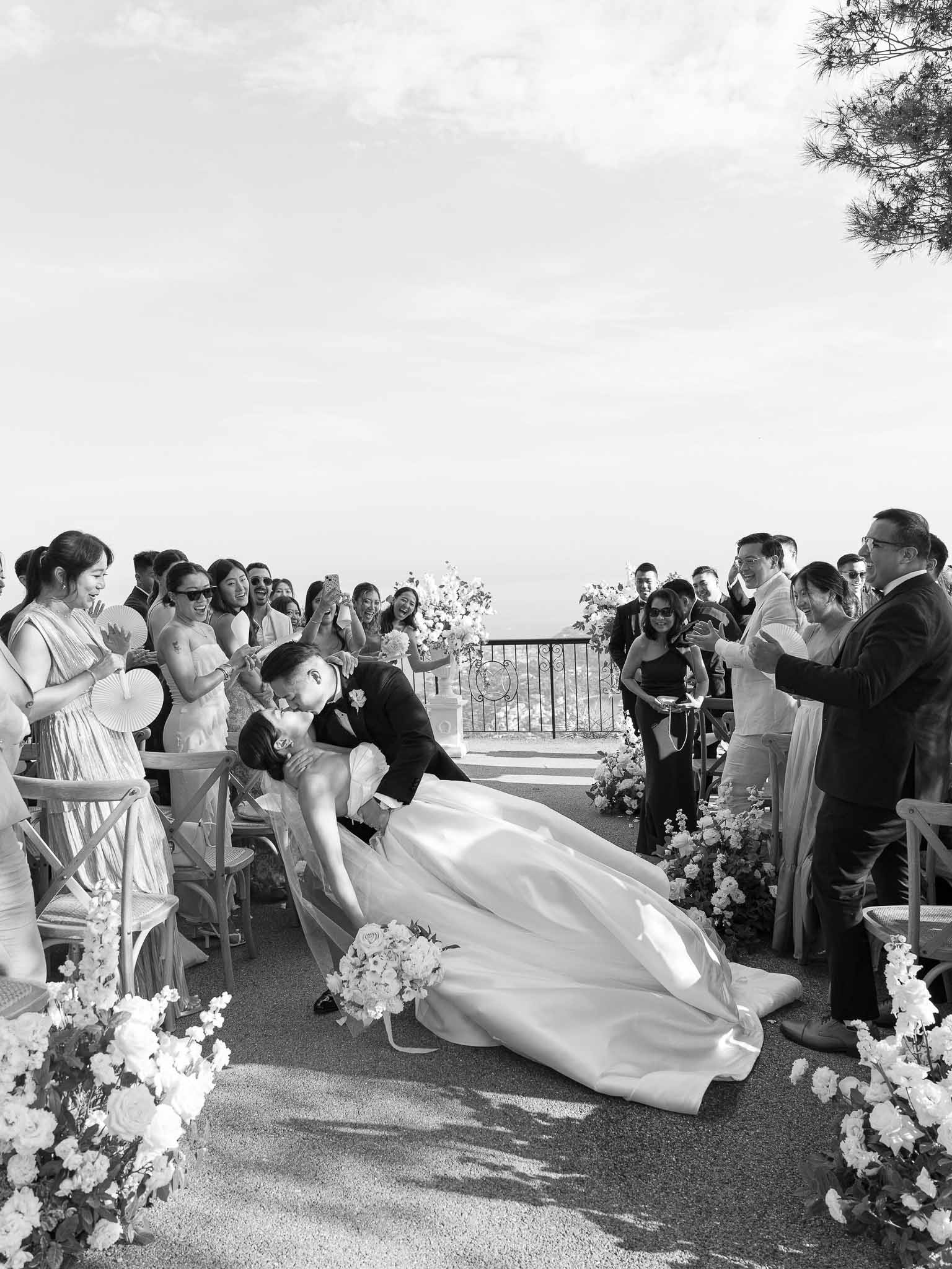Groom dipping bride during ceremony recessional on outdoor terrace with guests watching