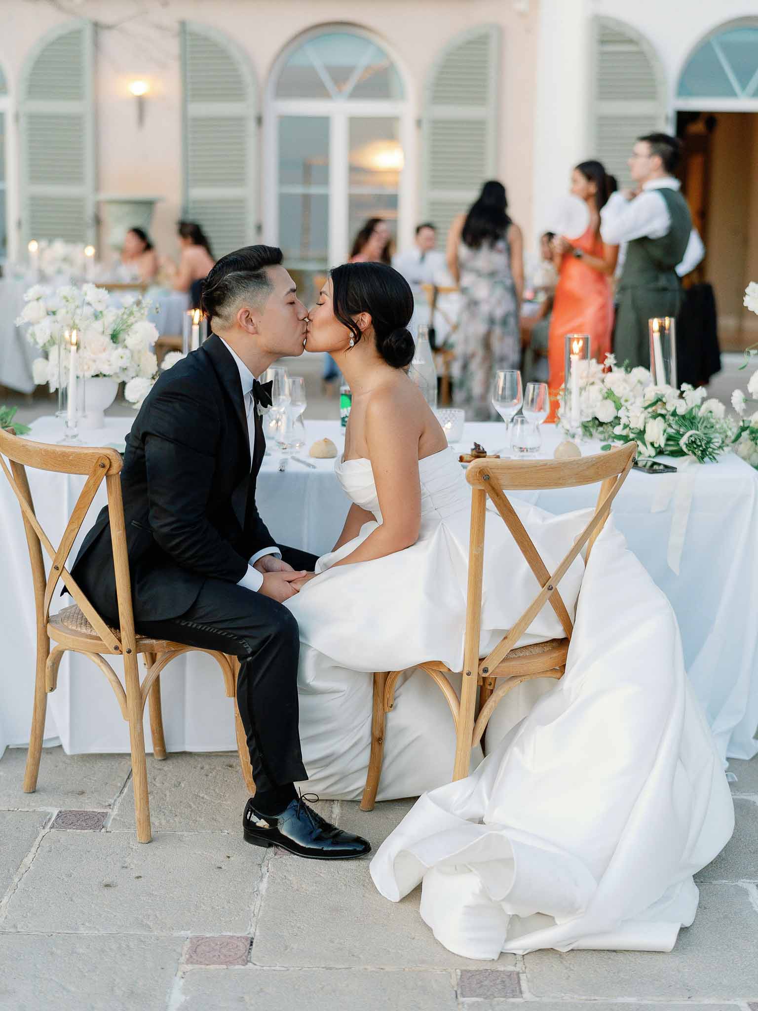 Bride and groom kissing at reception table in courtyard with stone columns and mint green shutters
