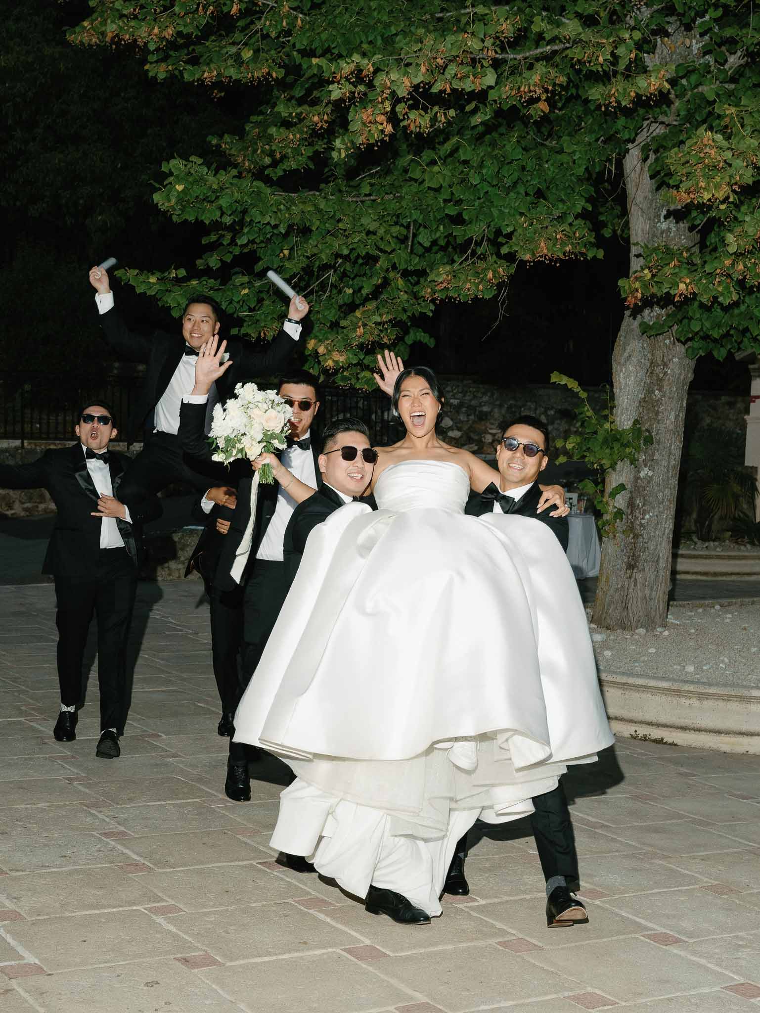 Bride being carried by groomsmen in celebration on outdoor stone terrace at wedding venue