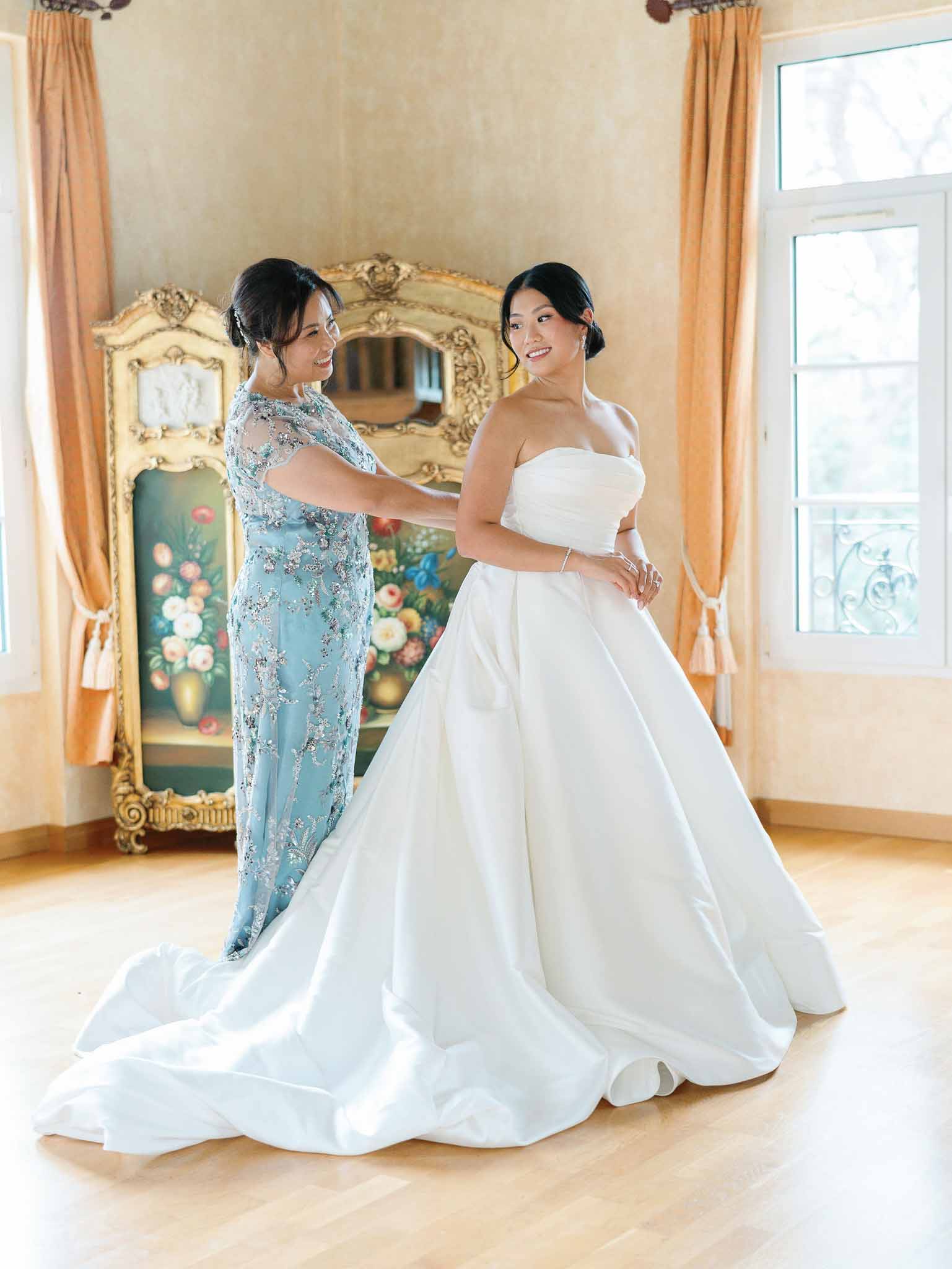 Bride in ivory ball gown with attendant in blue ao dai during getting ready at European château