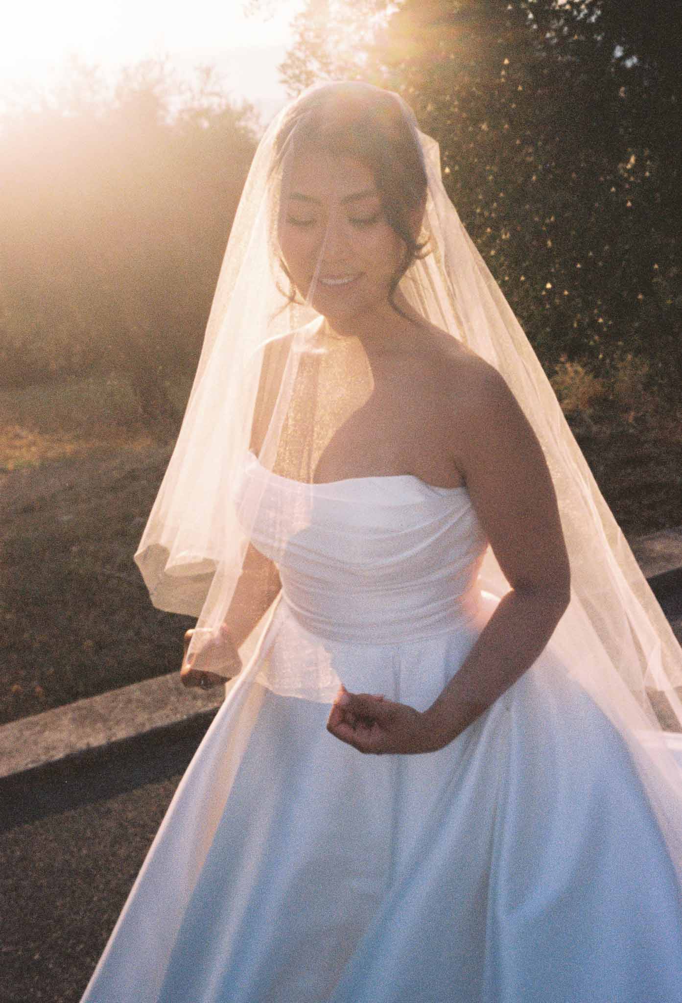 Bride in strapless white gown with ivory veil in outdoor garden setting during golden hour