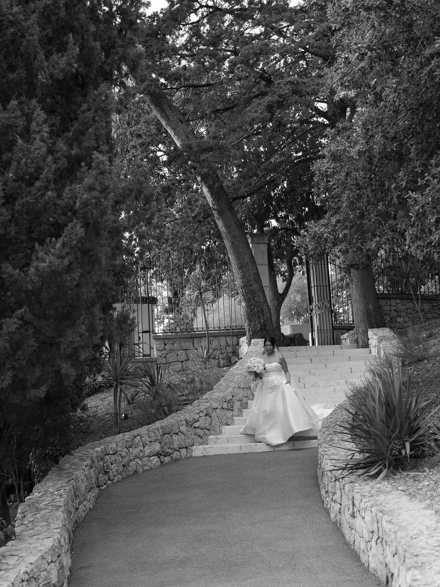 Bride in ball gown descending stone staircase at Mediterranean villa garden