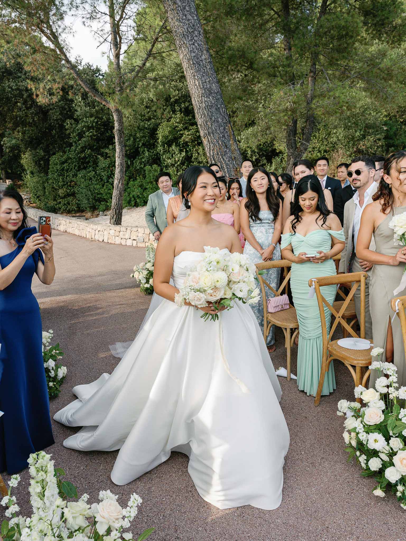 Bride walking down outdoor ceremony aisle with floral arrangements in garden setting