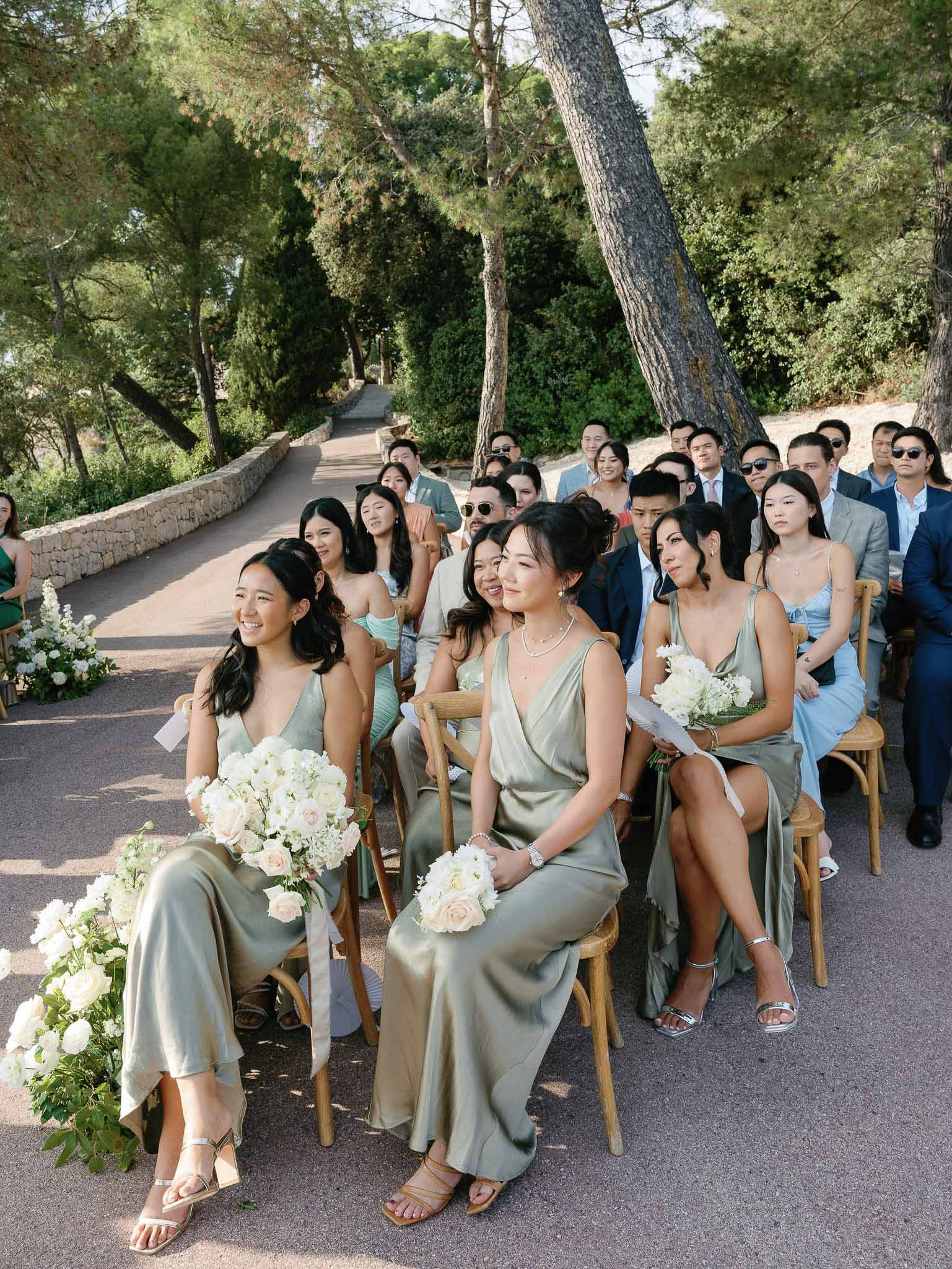 Outdoor wedding ceremony with guests seated on tree-lined stone pathway at Mediterranean-style estate