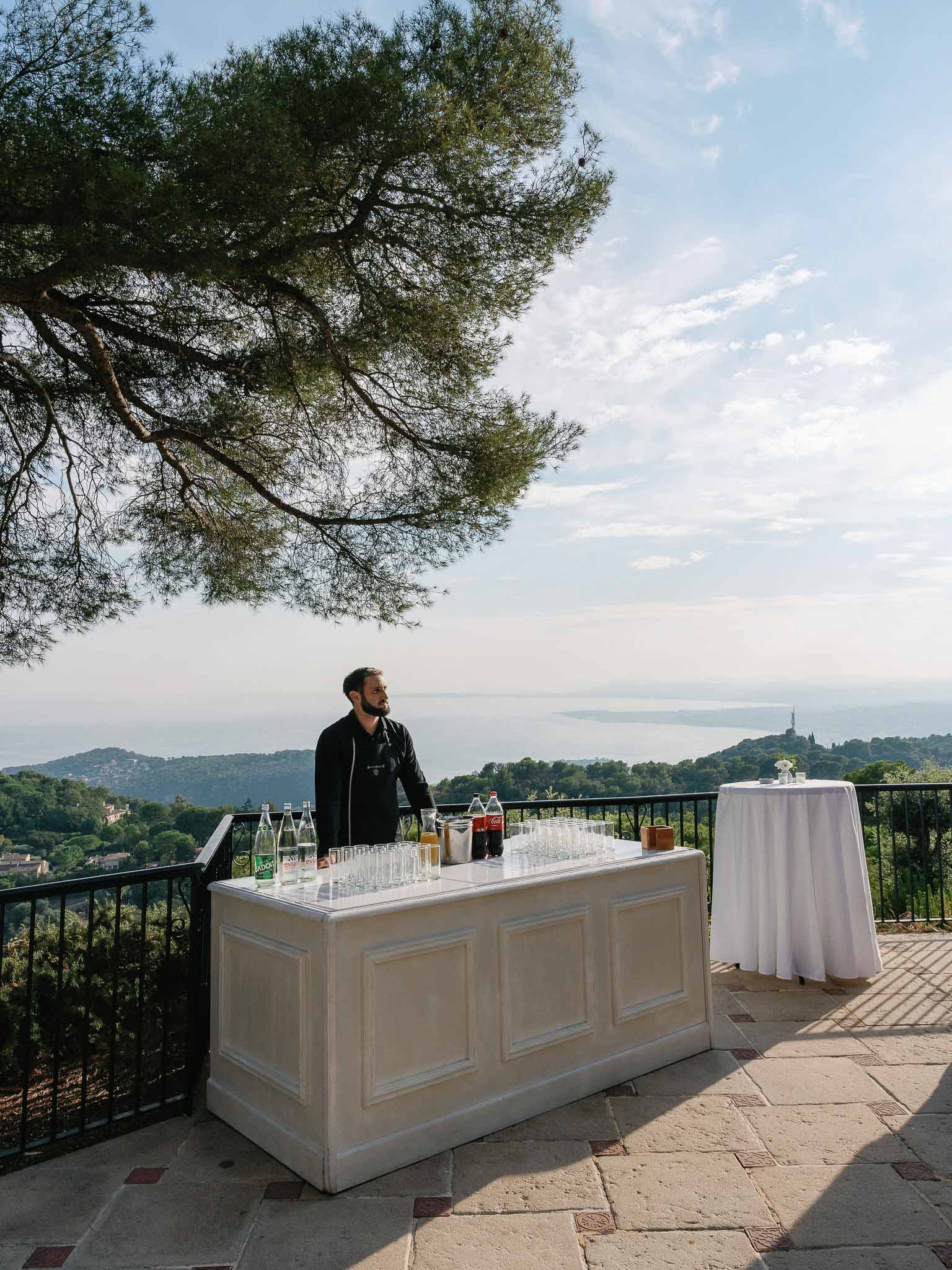 Bartender at outdoor terrace bar with Mediterranean landscape views during cocktail hour