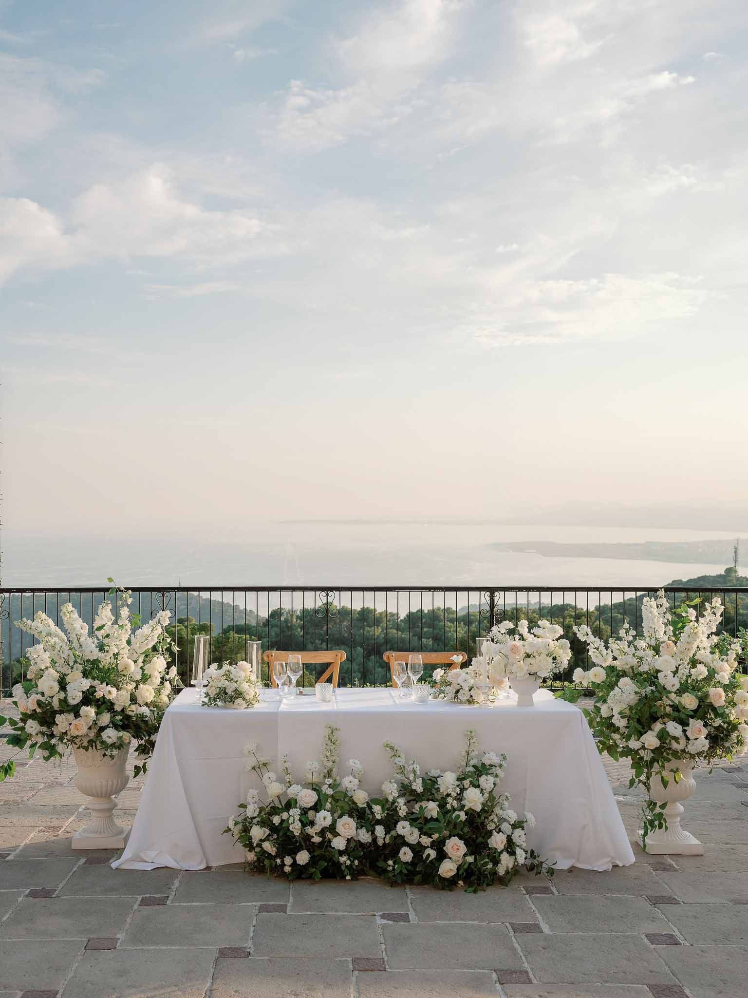 Sweetheart table with white florals on outdoor terrace overlooking landscape