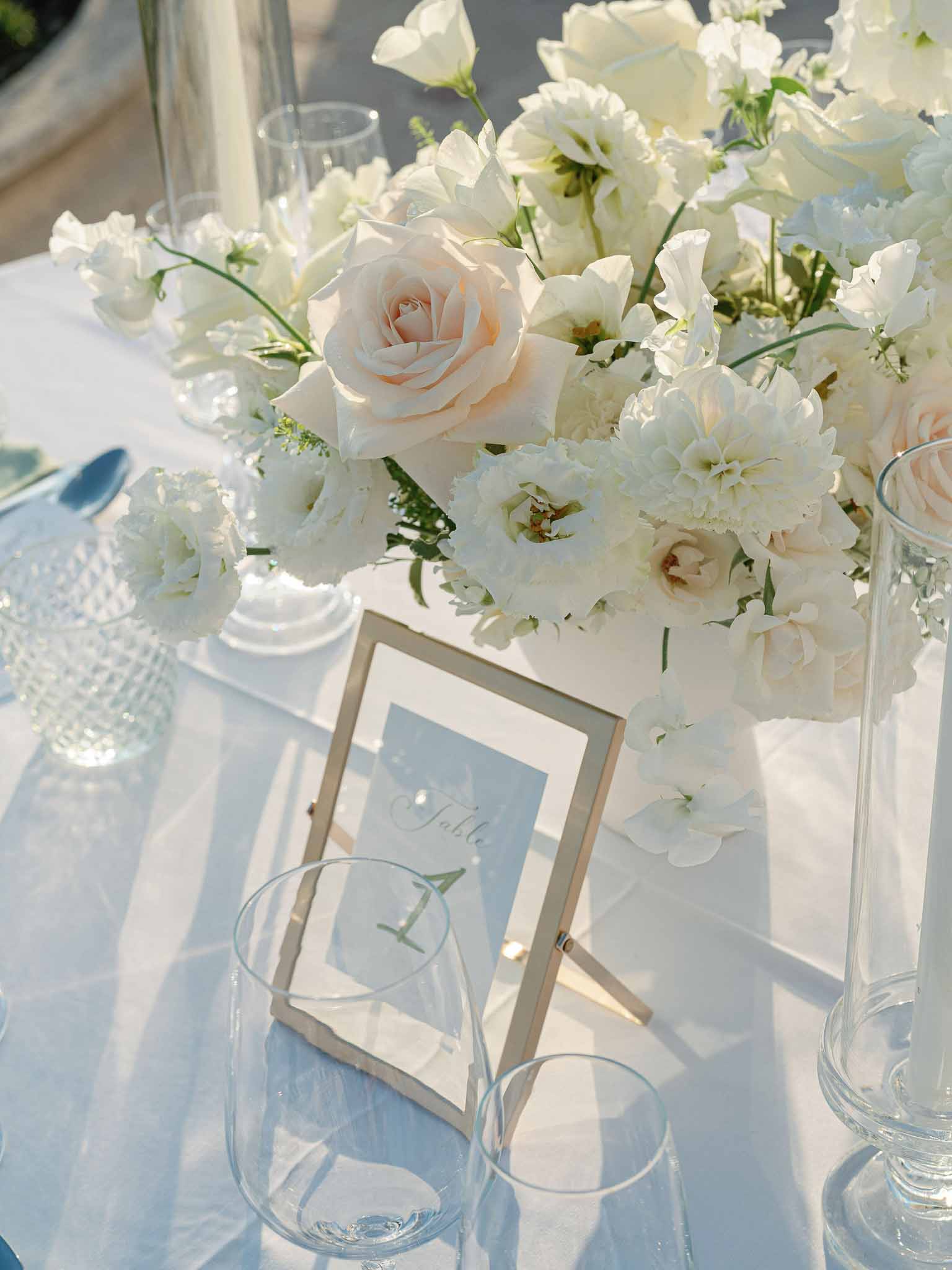 White glass centerpiece with ivory and blush flowers on reception table with clear glassware