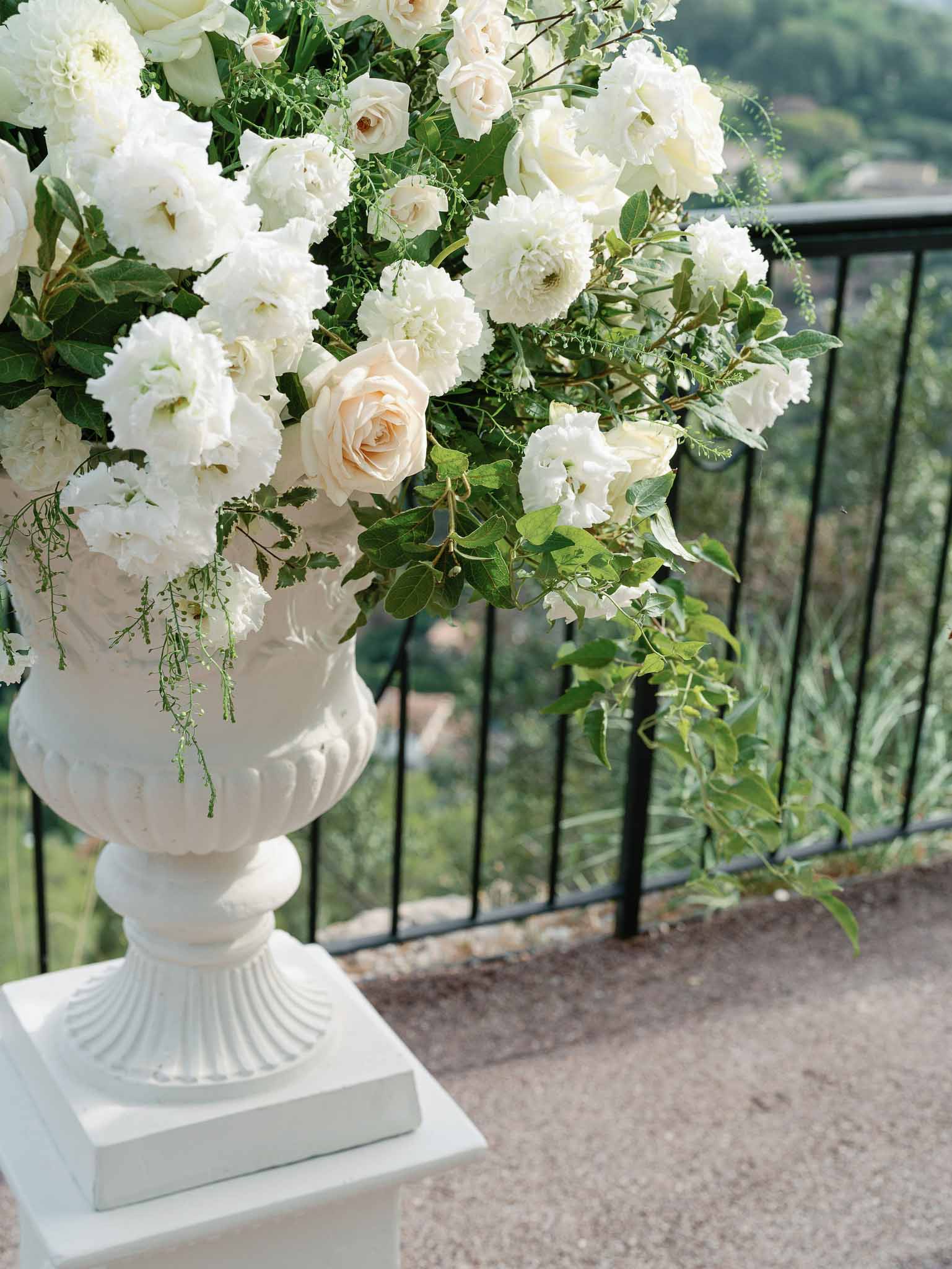 White floral arrangement in pedestal urn with peonies and roses at outdoor wedding venue terrace