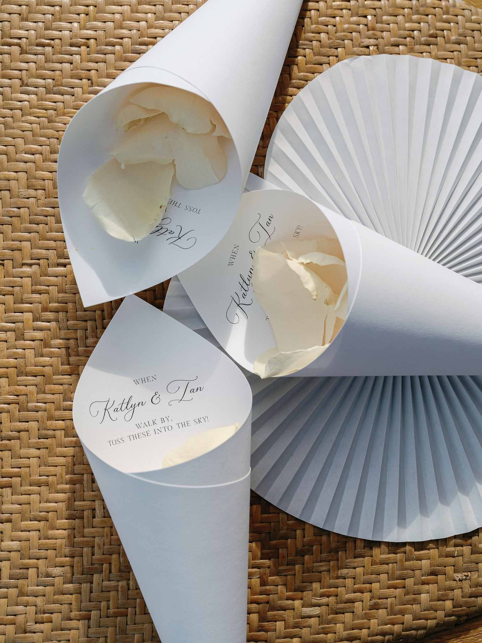 Wedding favor petal toss cones with couple names arranged on woven surface