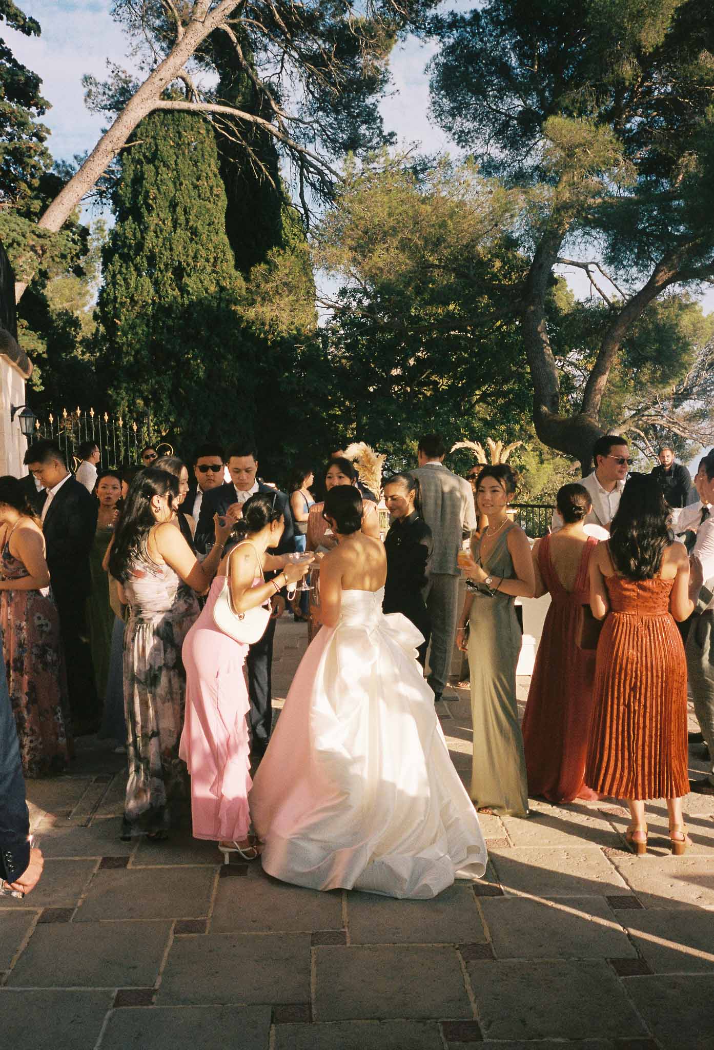 Outdoor cocktail hour with guests mingling on stone patio under mature trees at garden estate venue