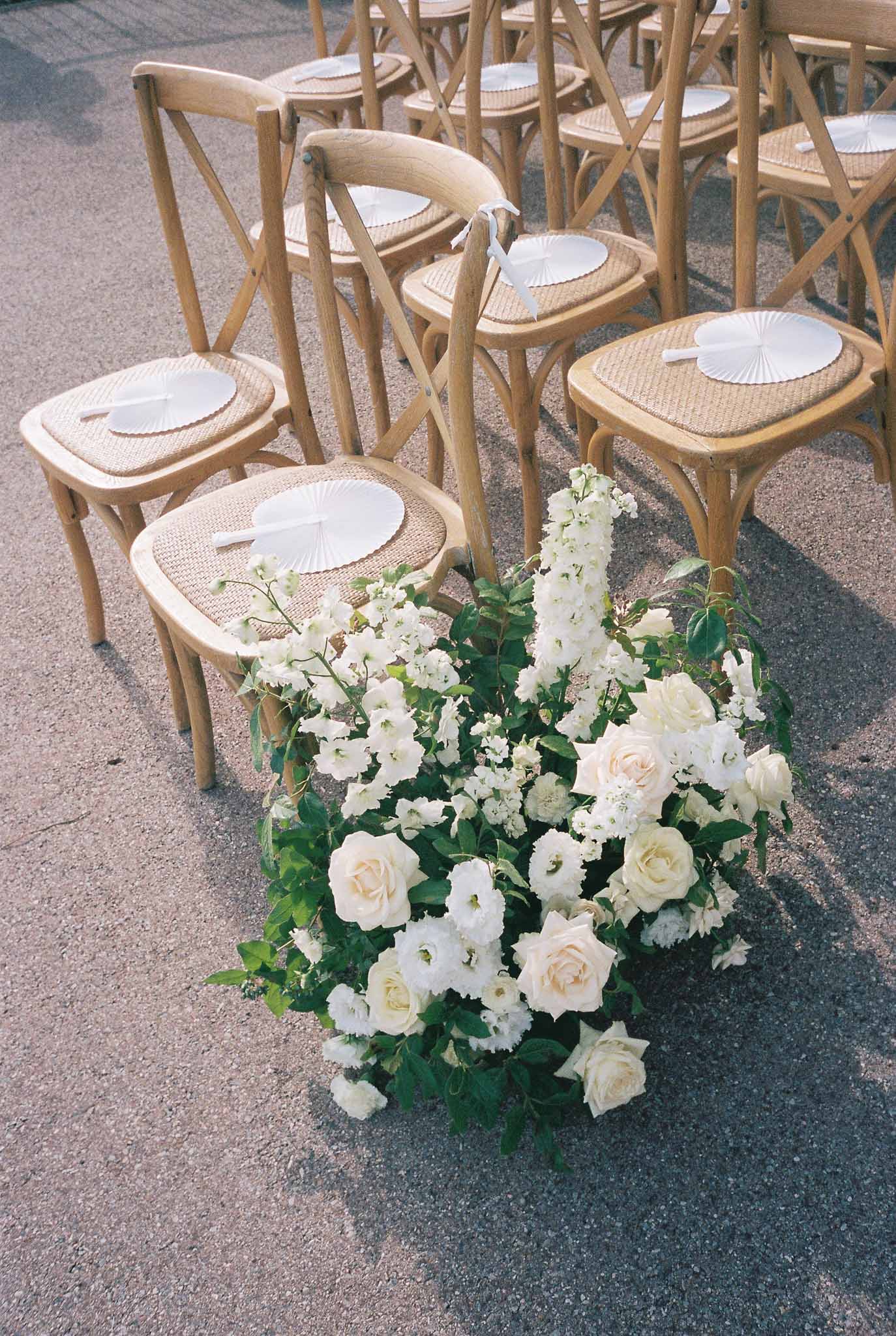Wedding ceremony seating with wooden chairs, white programs, and cream floral arrangements