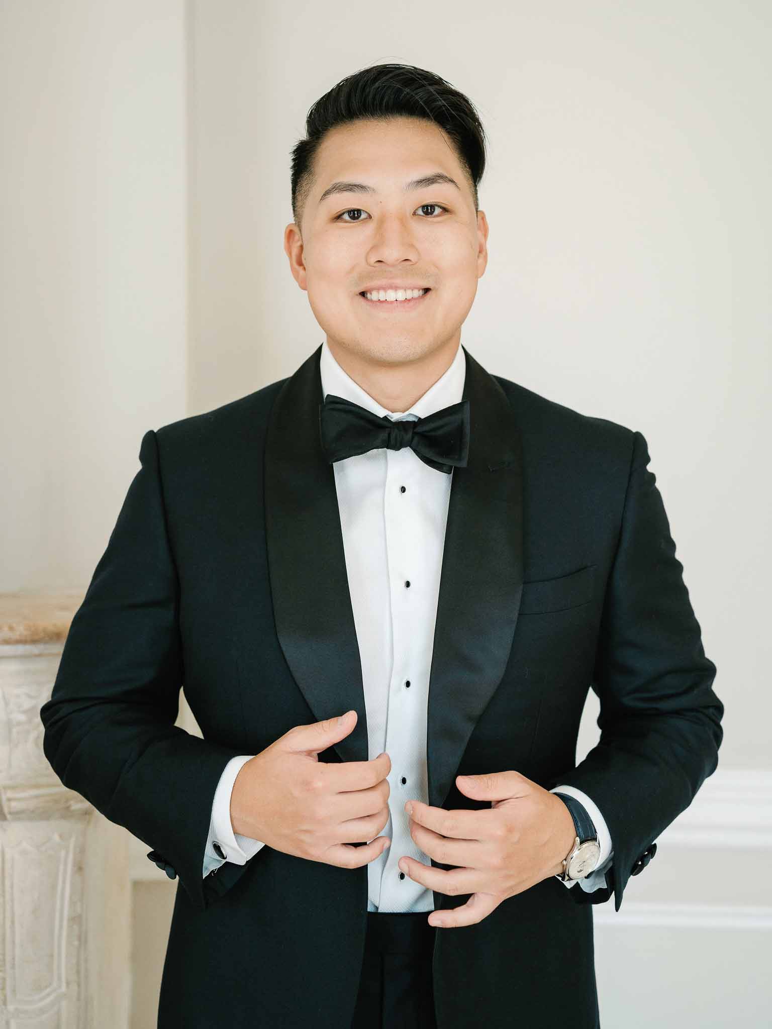 Groom in black tuxedo and bow tie portrait against neutral wall