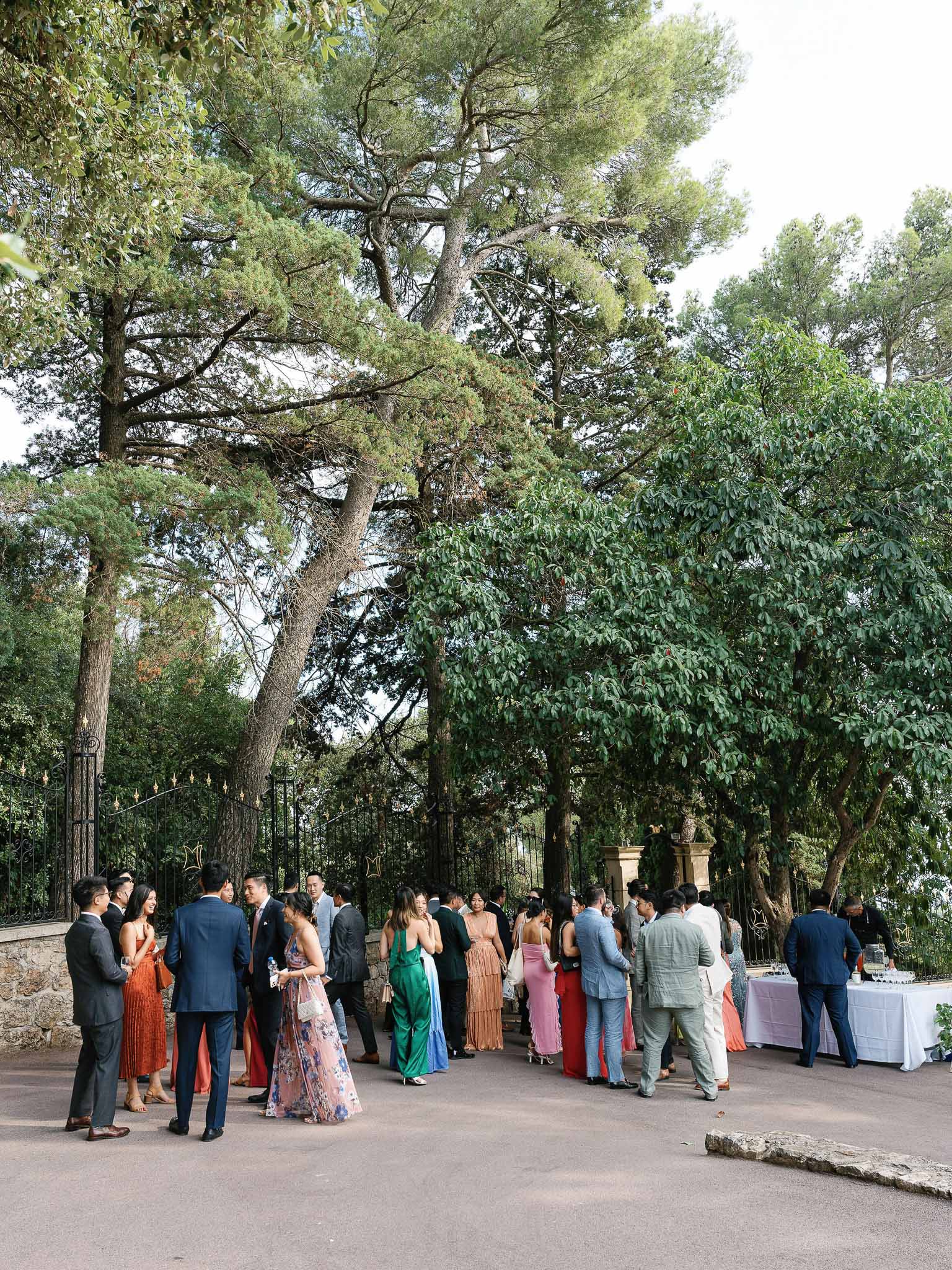 Cocktail hour reception with guests mingling in tree-lined garden courtyard at Mediterranean venue