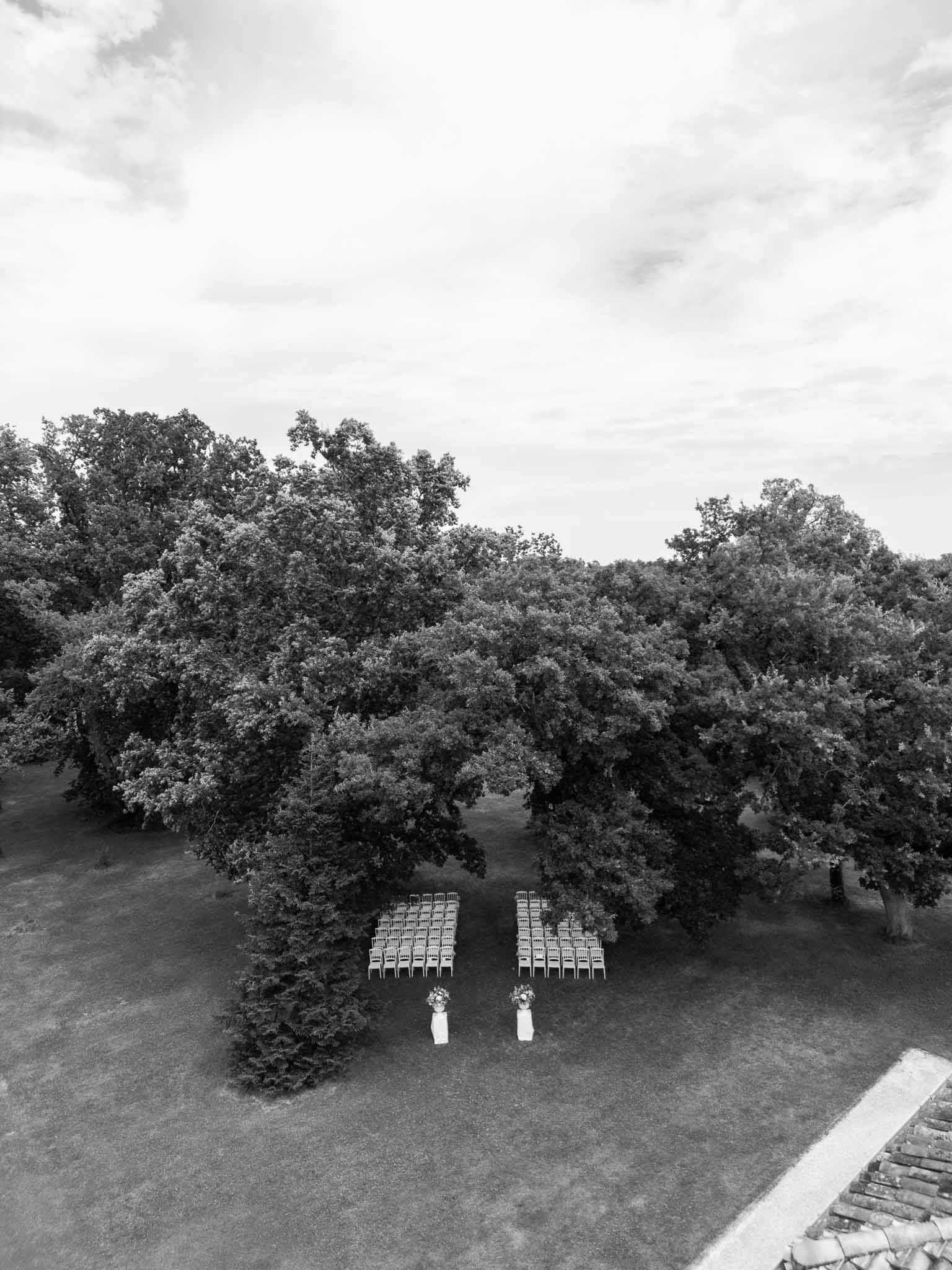 Aerial view of outdoor wedding ceremony setup with white chairs arranged in woodland clearing