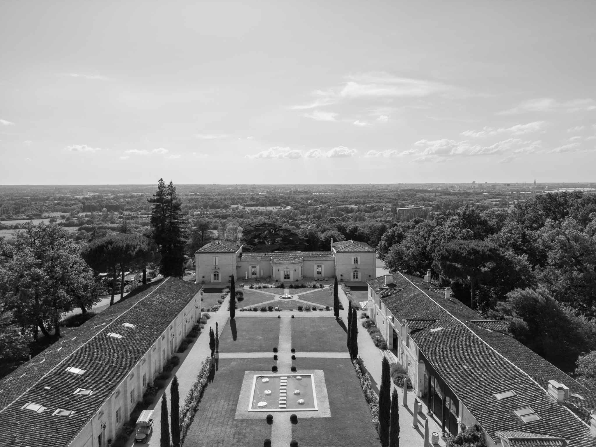 Aerial view of classical manor house estate with formal gardens and distant city skyline