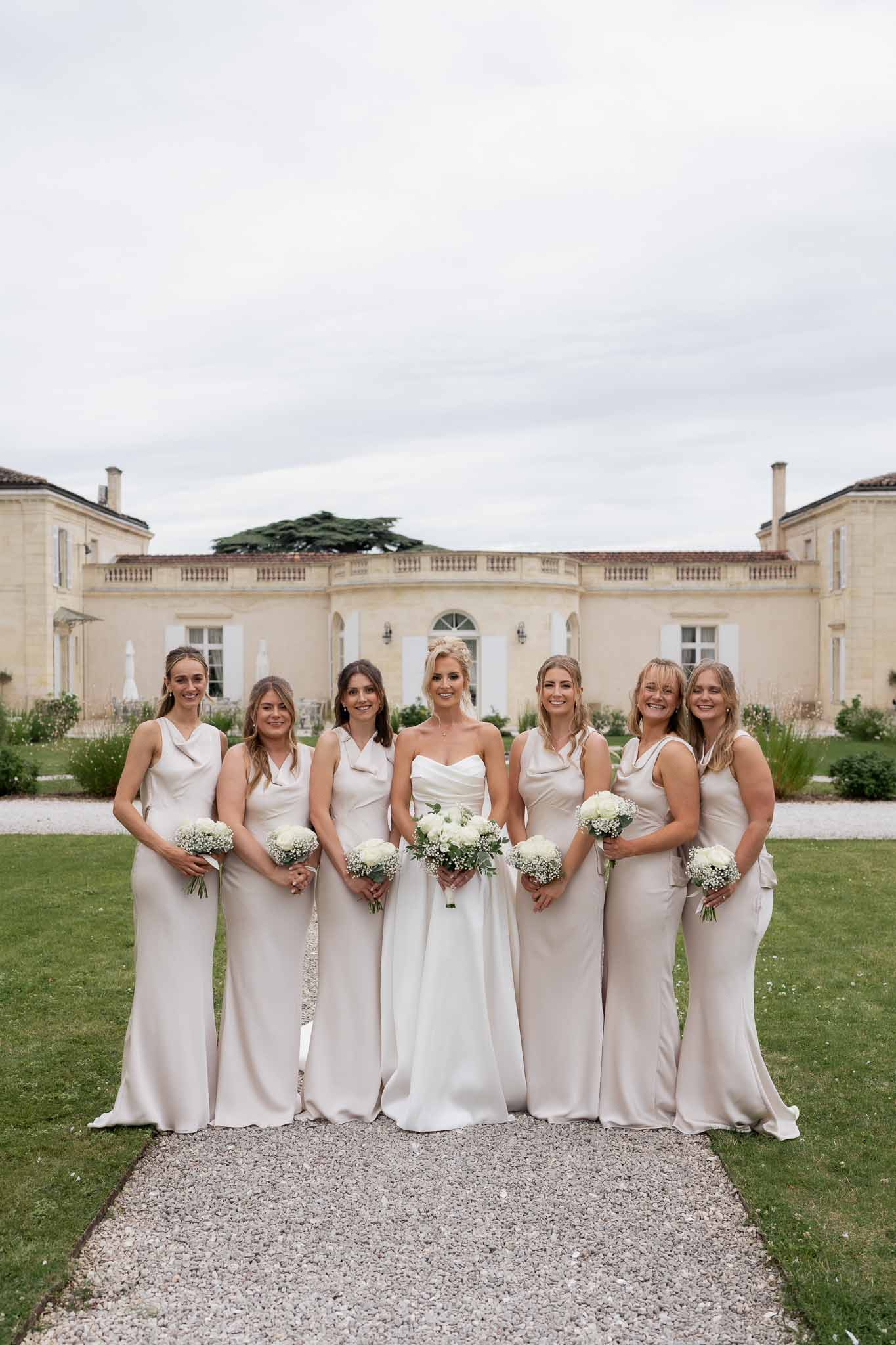 Bride and bridesmaids group portrait on mansion lawn with classical stone building
