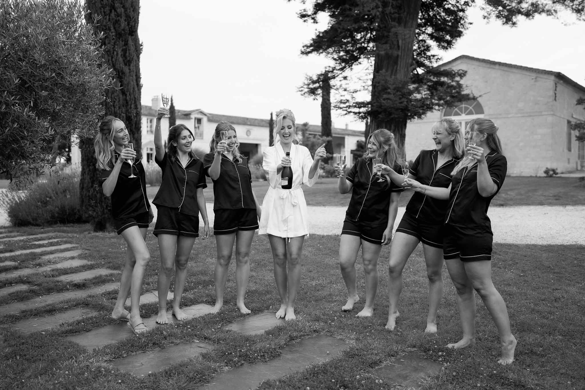 Bridal party portrait with bride and bridesmaids holding champagne glasses in villa courtyard