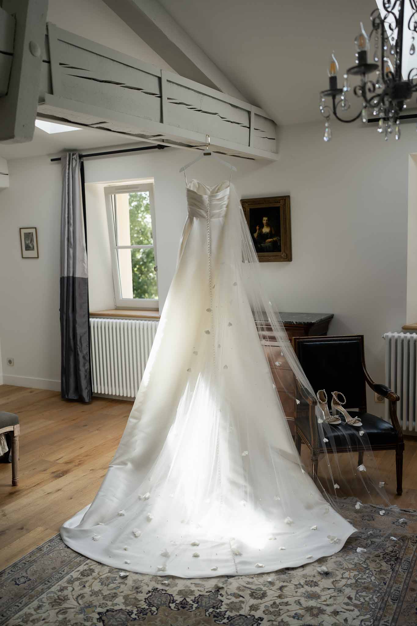 Ivory wedding dress with chapel train hanging in elegant preparation room with classic European decor