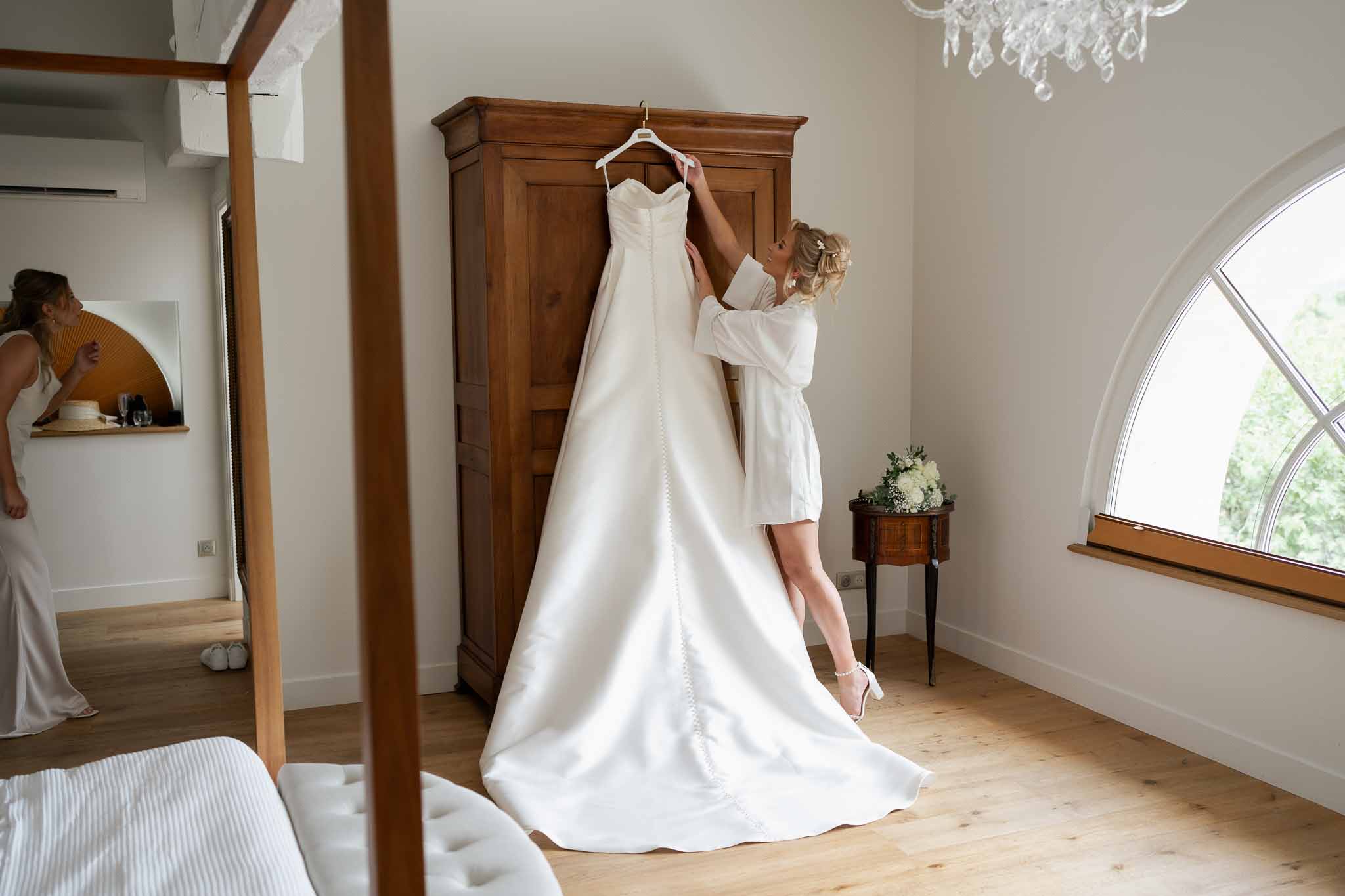 Bride displaying wedding dress on hanger in classical bedroom during getting ready preparations