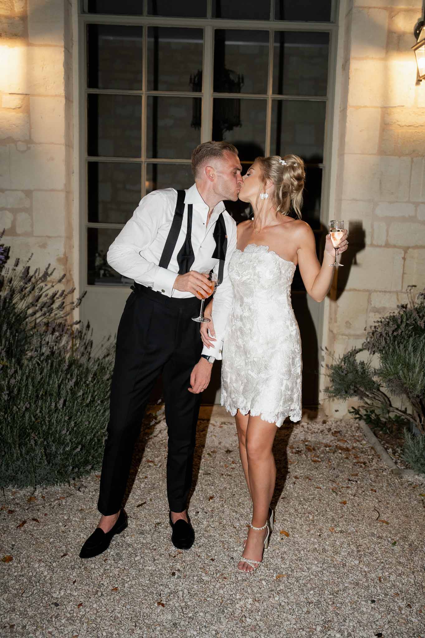 Bride and groom kissing during evening reception in stone courtyard at classical venue