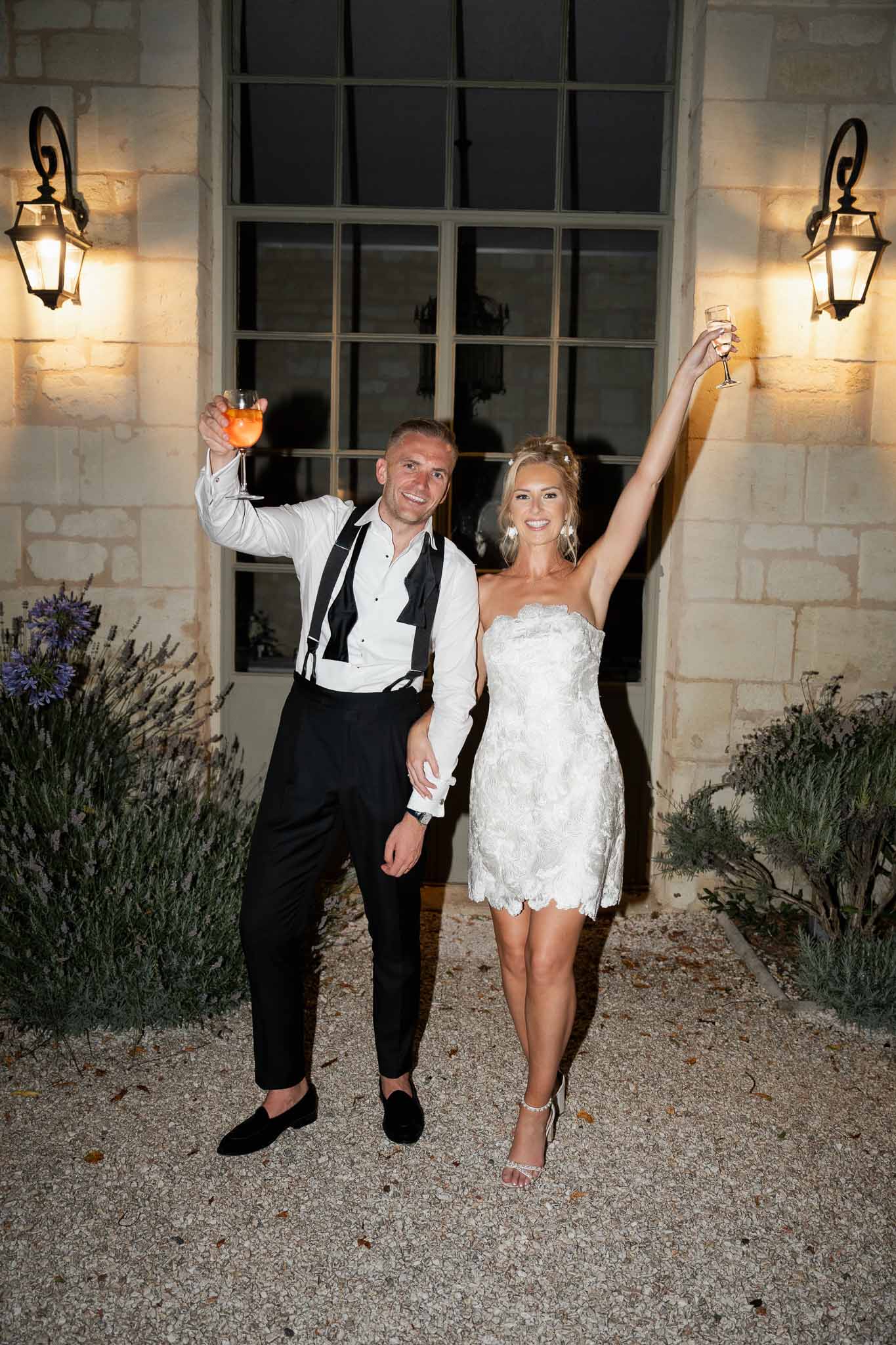 Bride and groom toasting with champagne glasses at night outside stone building with lavender courtyard