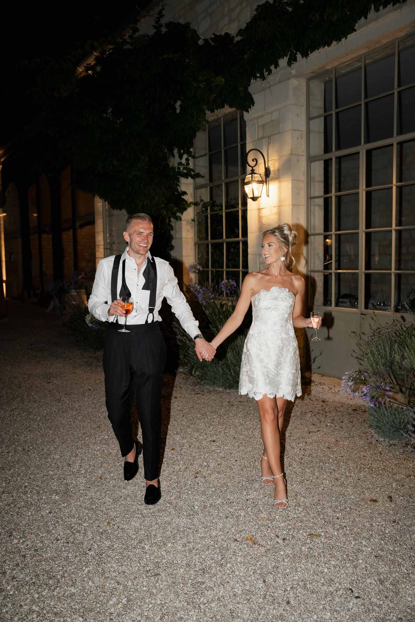 Bride and groom walking hand-in-hand in courtyard at night during wedding reception