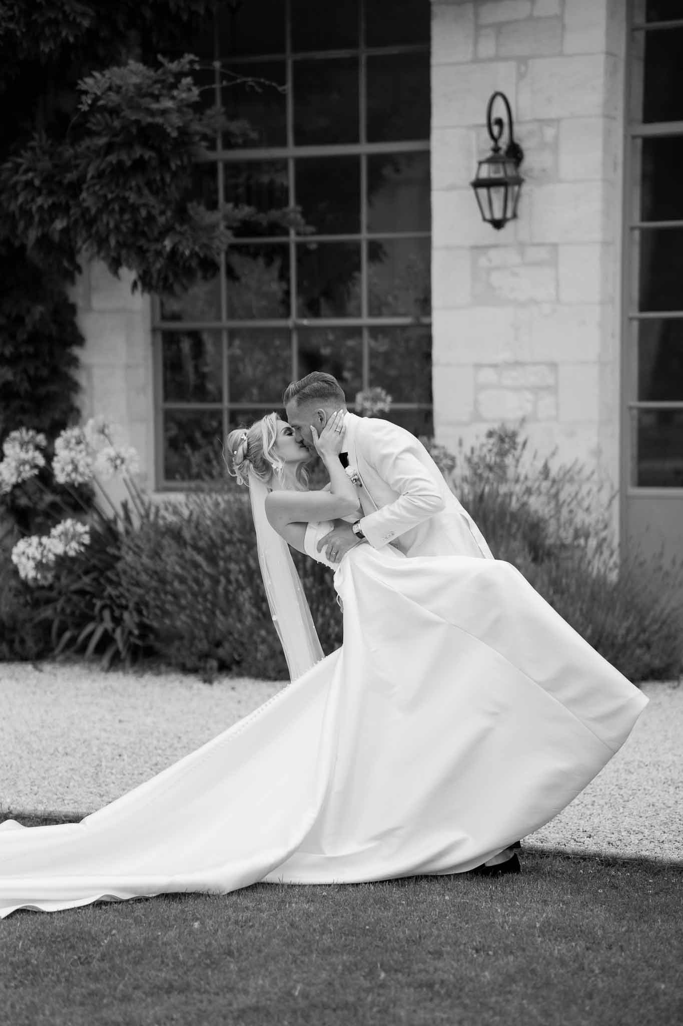 Groom dipping and kissing bride in formal courtyard with stone building backdrop