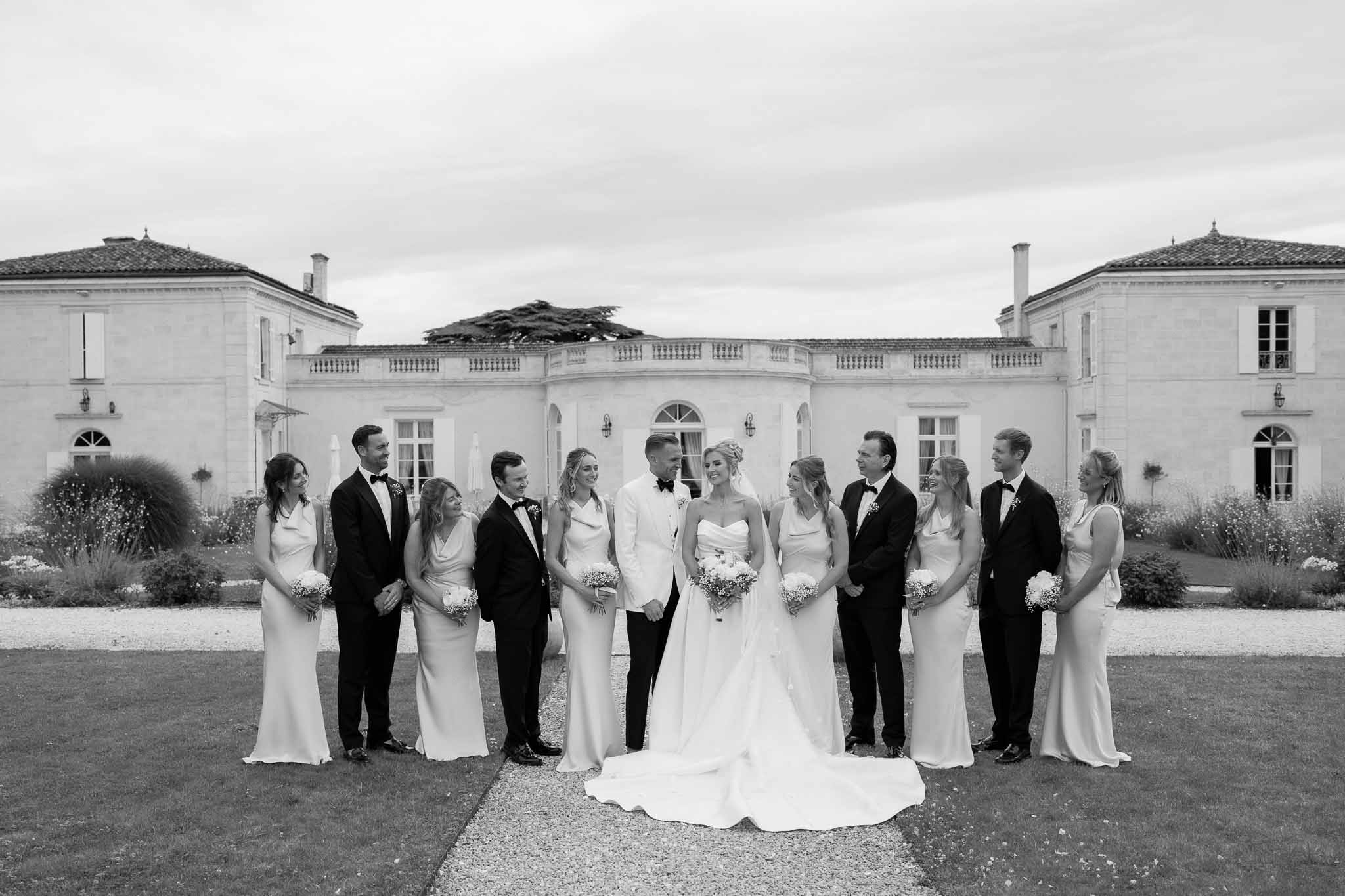 Formal bridal party portrait in front of classical white stone mansion with bride, groom, bridesmaids and groomsmen
