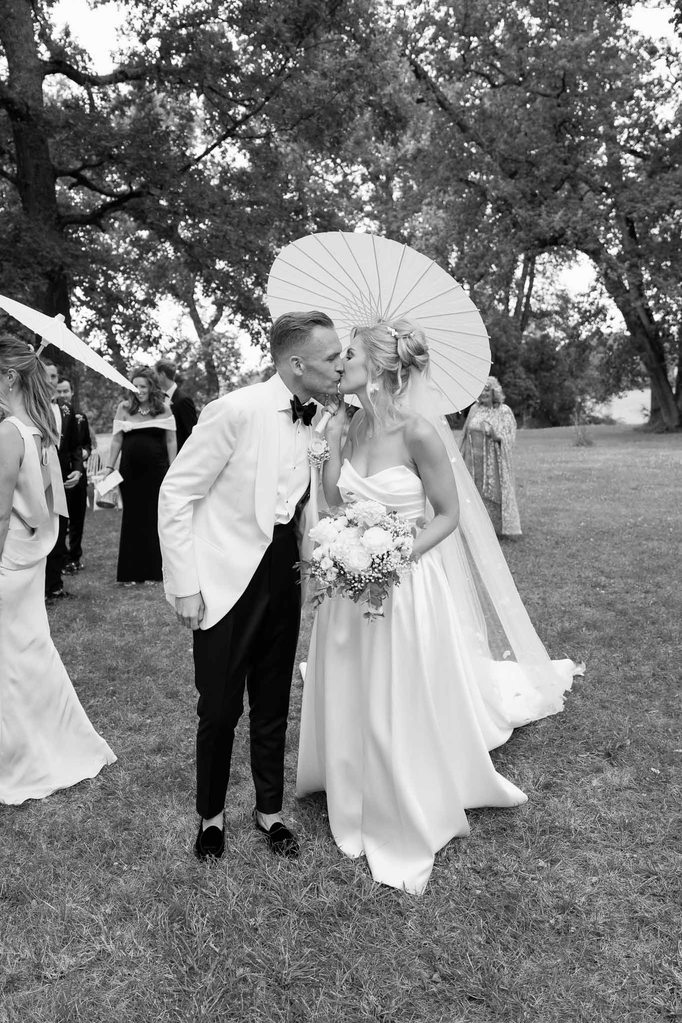 Couple kissing during outdoor garden reception with guests in background