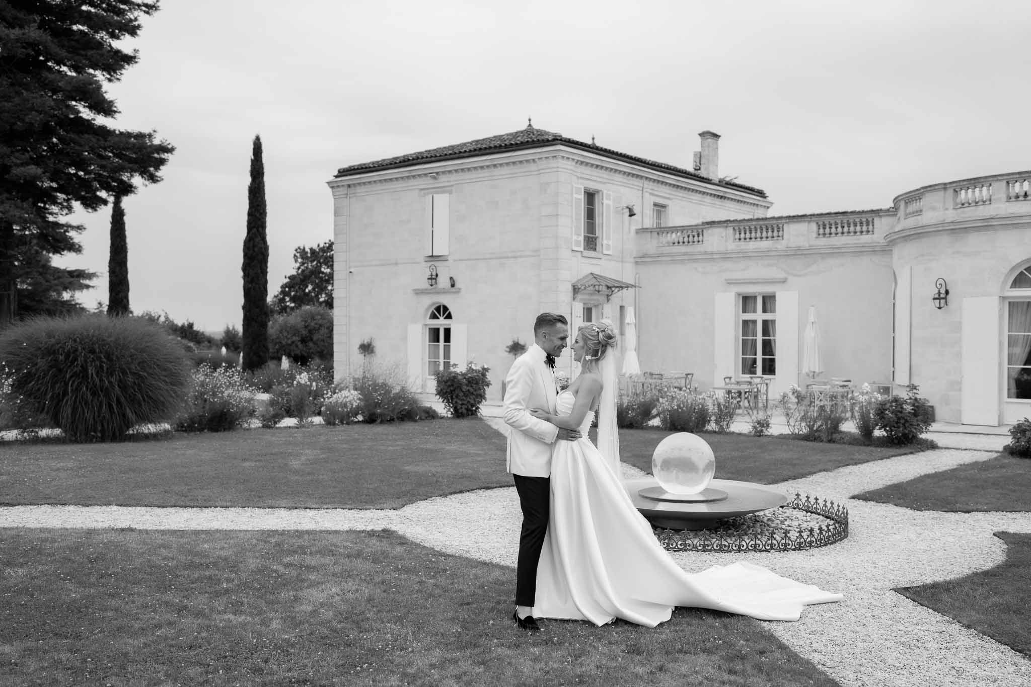 Bride and groom posing in front of neoclassical mansion with formal gardens