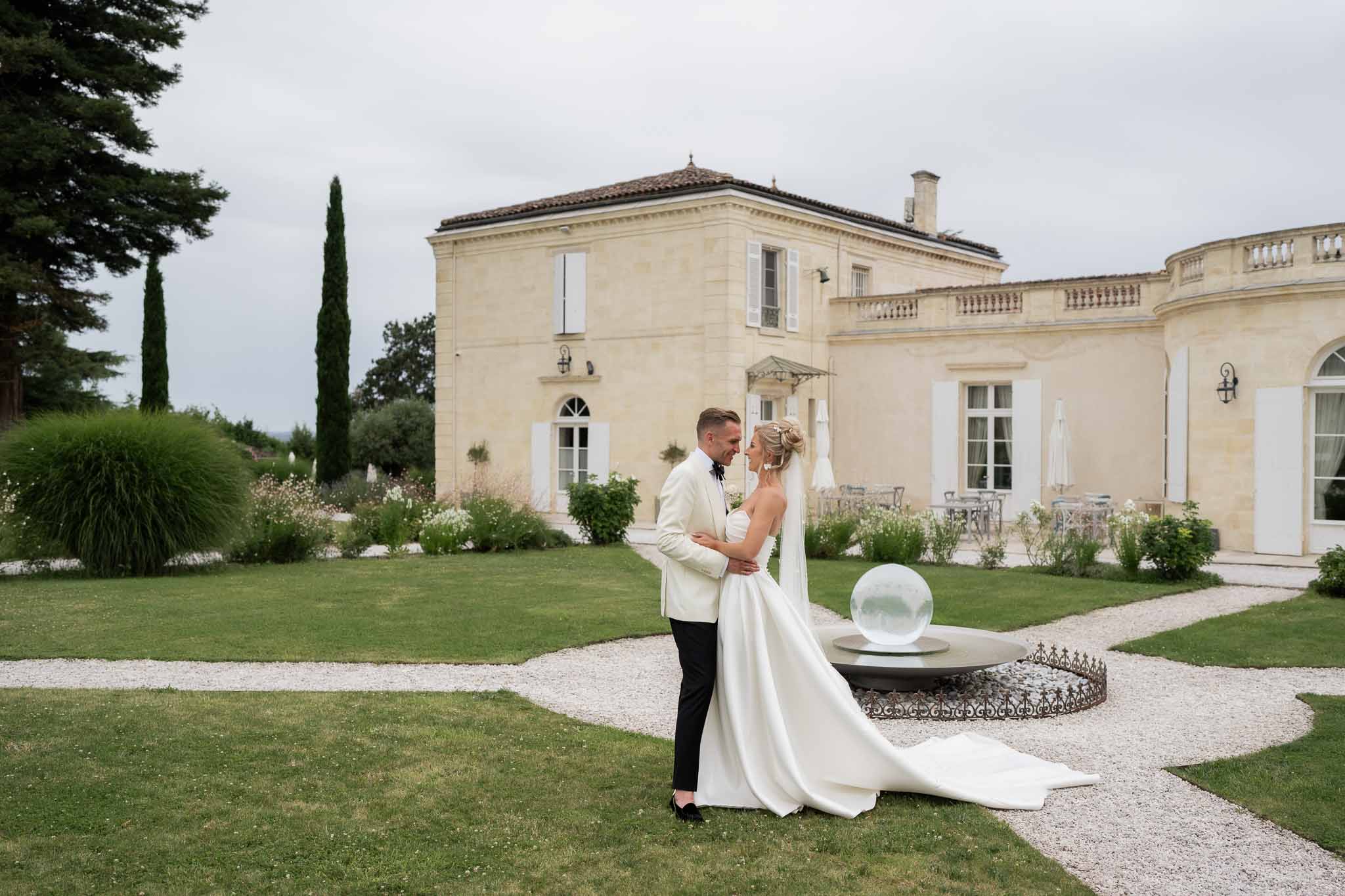 Bride and groom portrait on manicured lawn at classical stone chateau with formal gardens