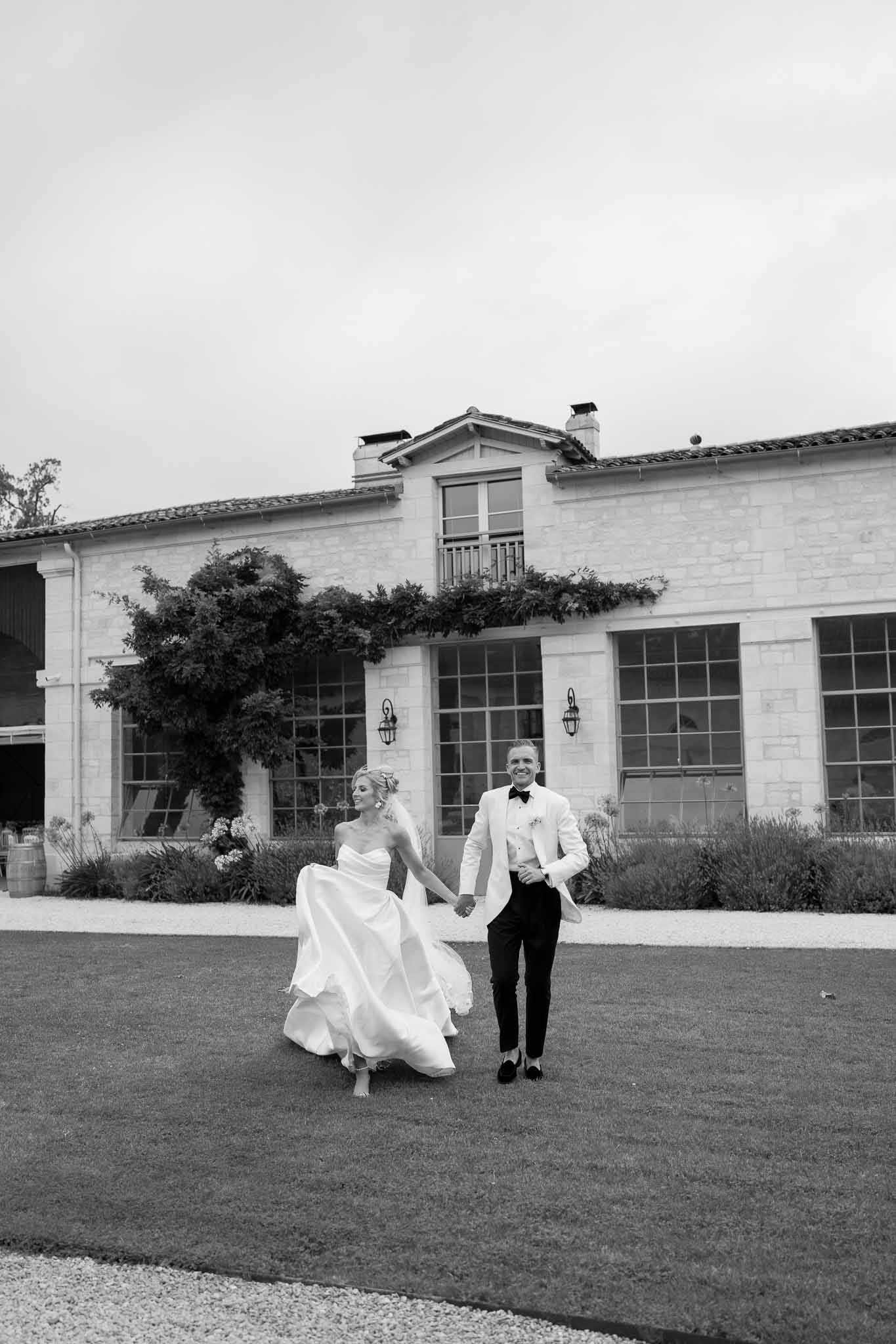 Newlywed couple walking hand-in-hand across courtyard at modern farmhouse wedding venue