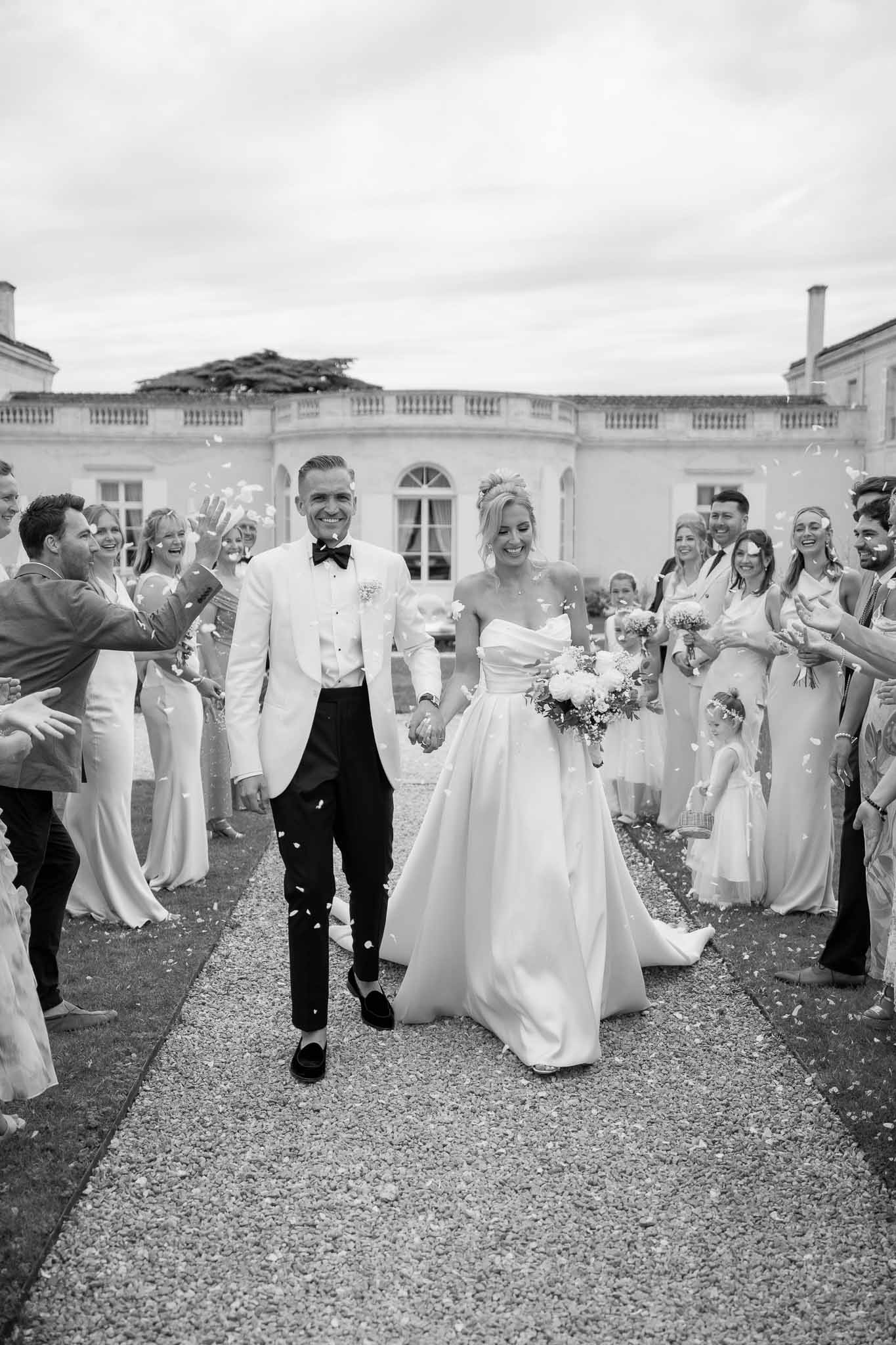 Bride and groom recessional with guests tossing petals at neoclassical mansion courtyard
