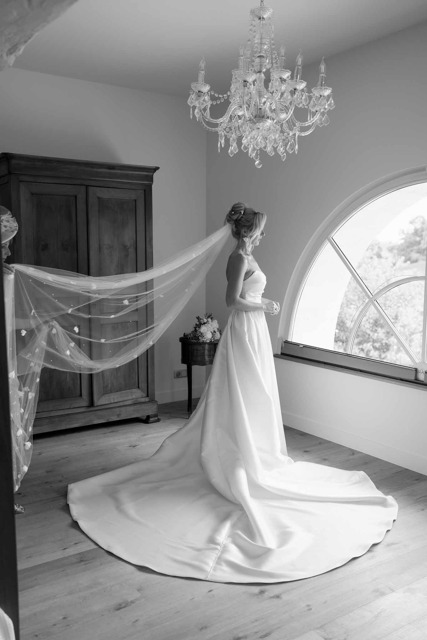 Bride in profile holding bouquet by arched window in elegant interior room