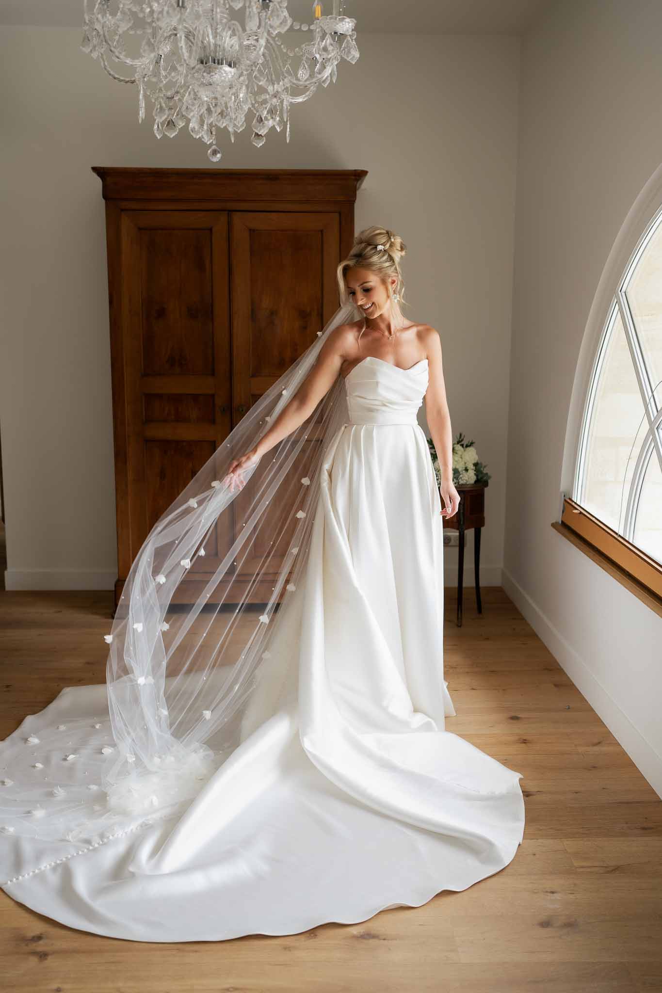 Bride in white gown with cathedral veil posing in elegant indoor bridal suite