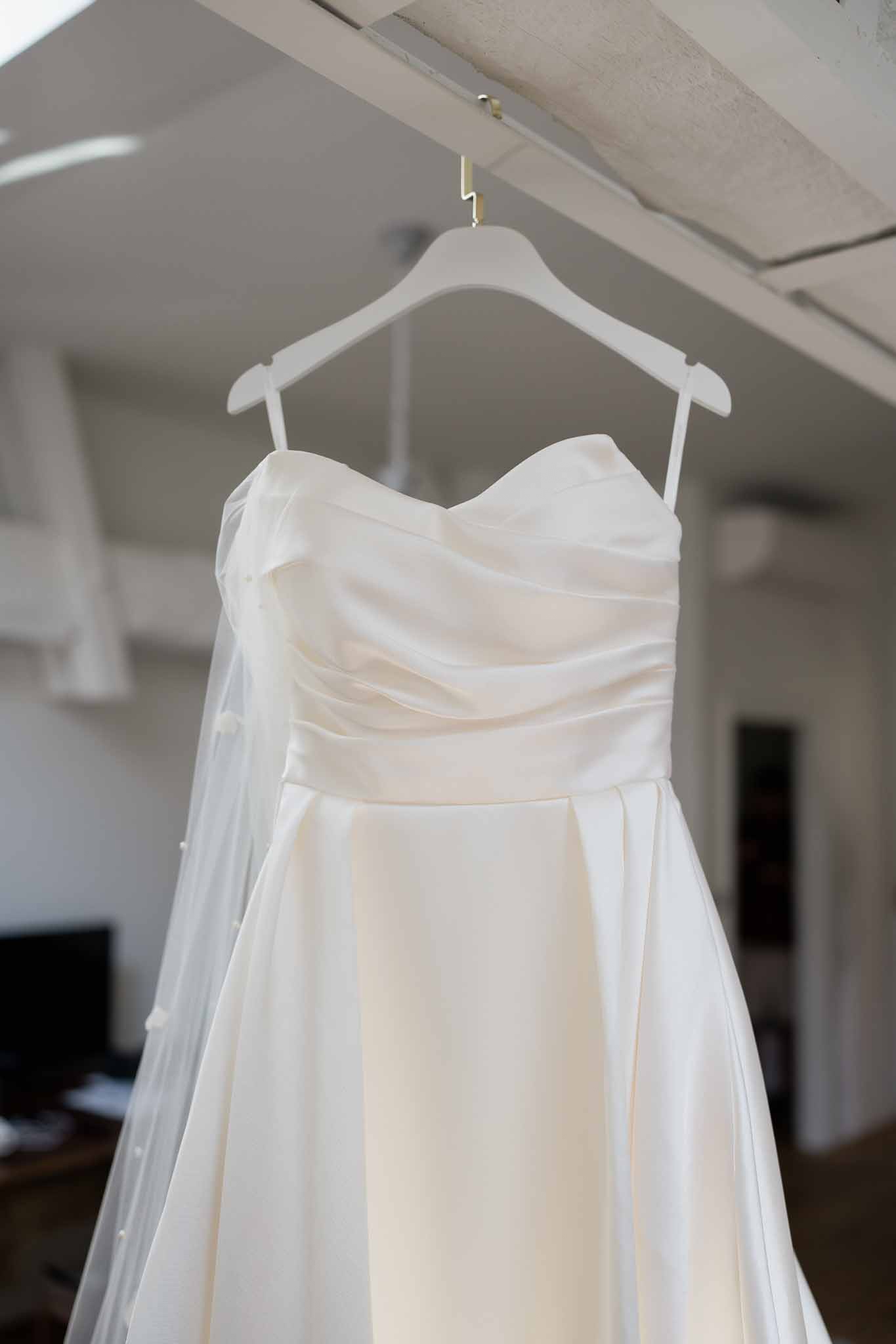 Ivory wedding dress hanging on wooden hanger in bridal getting ready room