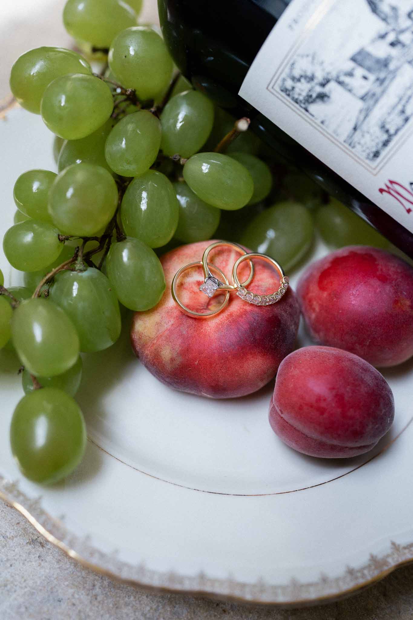 Wedding rings displayed on red apple with grapes and wine bottle in flat lay composition
