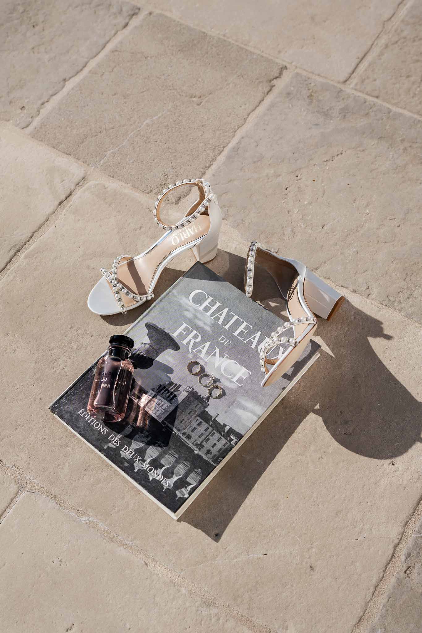 Flat lay of white bridal sandals, perfume bottle and magazine on stone surface with natural shadows