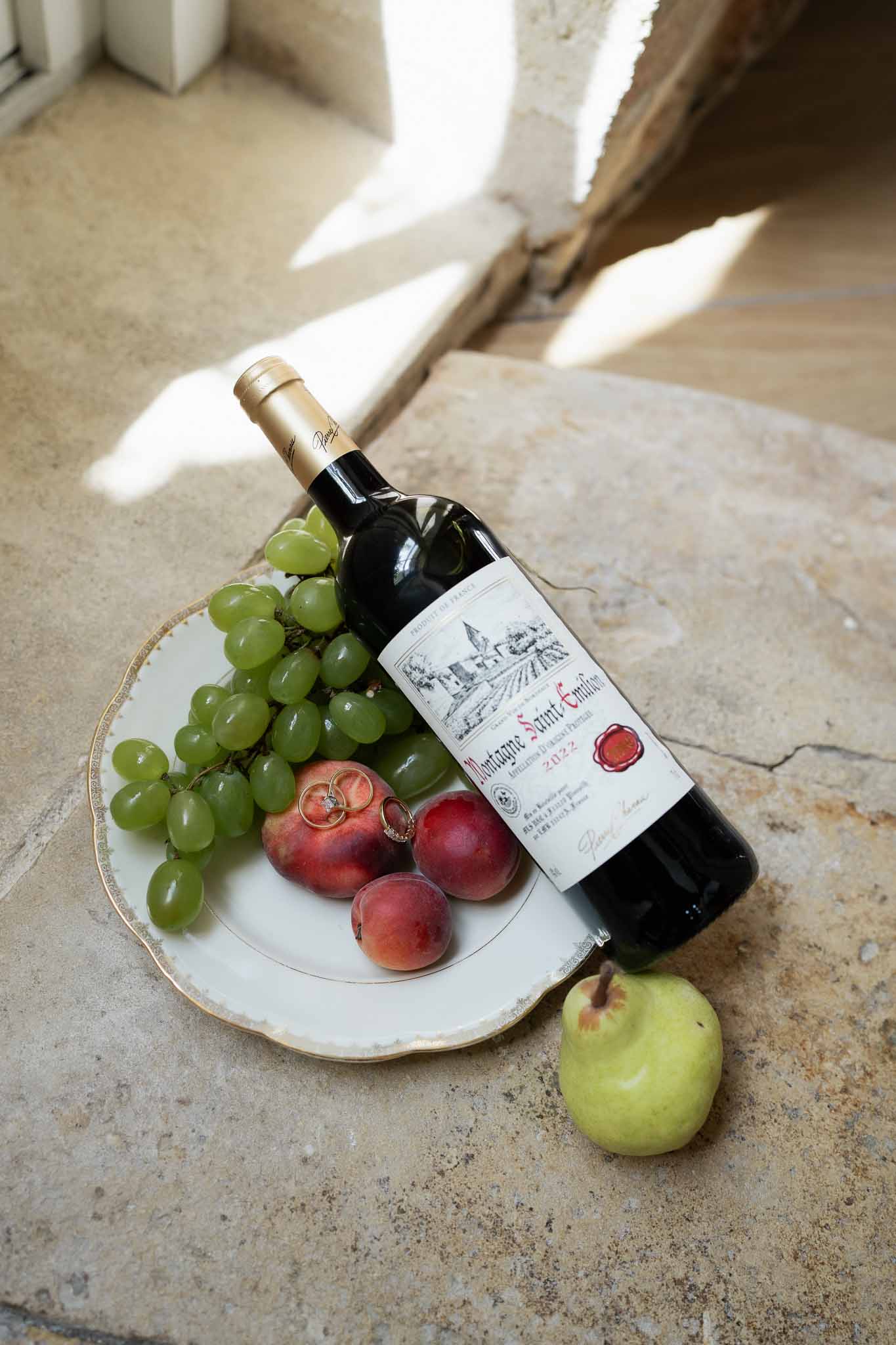 Wedding rings on pomegranates with Bordeaux wine bottle flat lay on stone floor