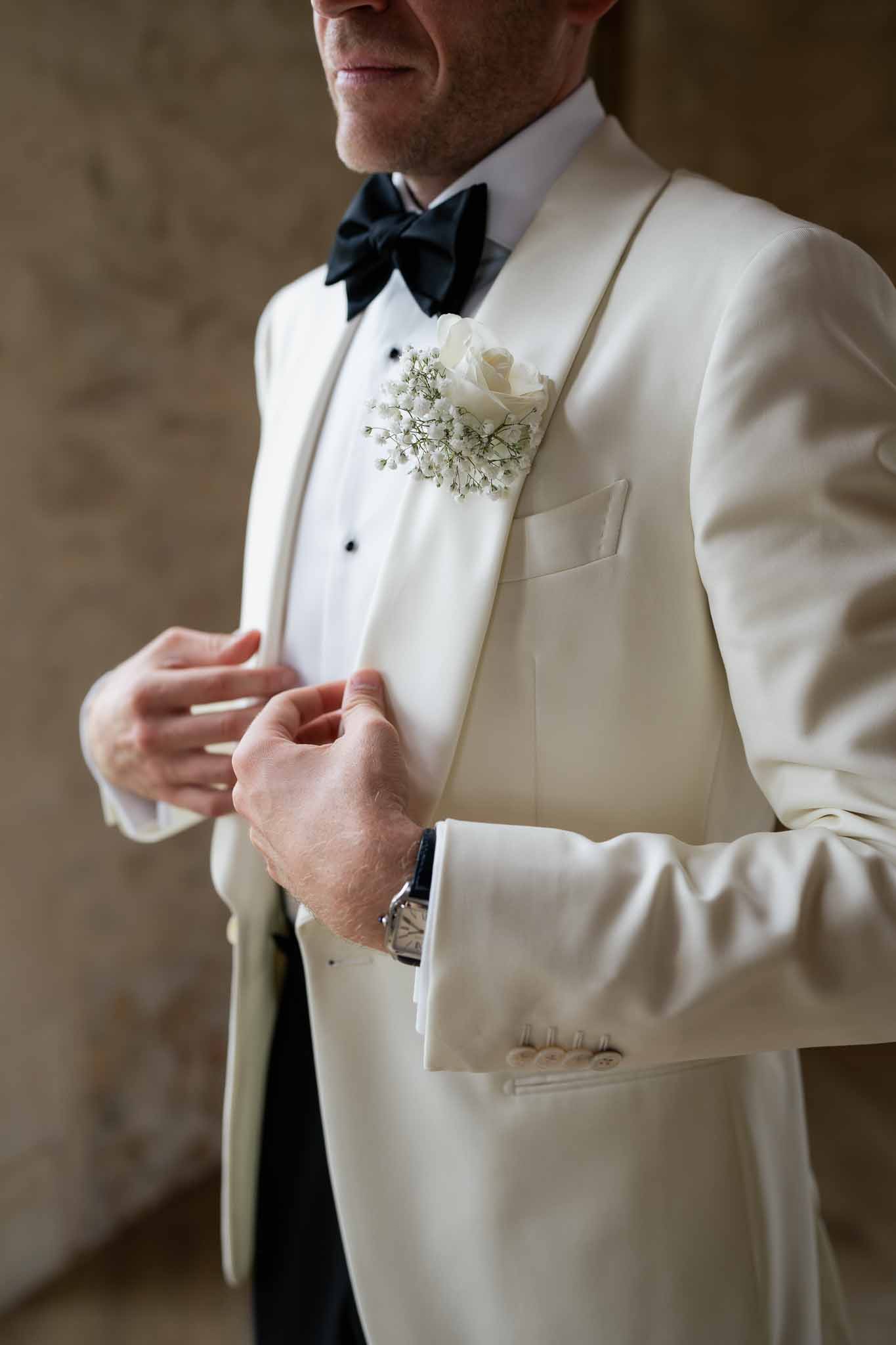 Groom in cream tuxedo with navy bow tie and ivory boutonnière indoors