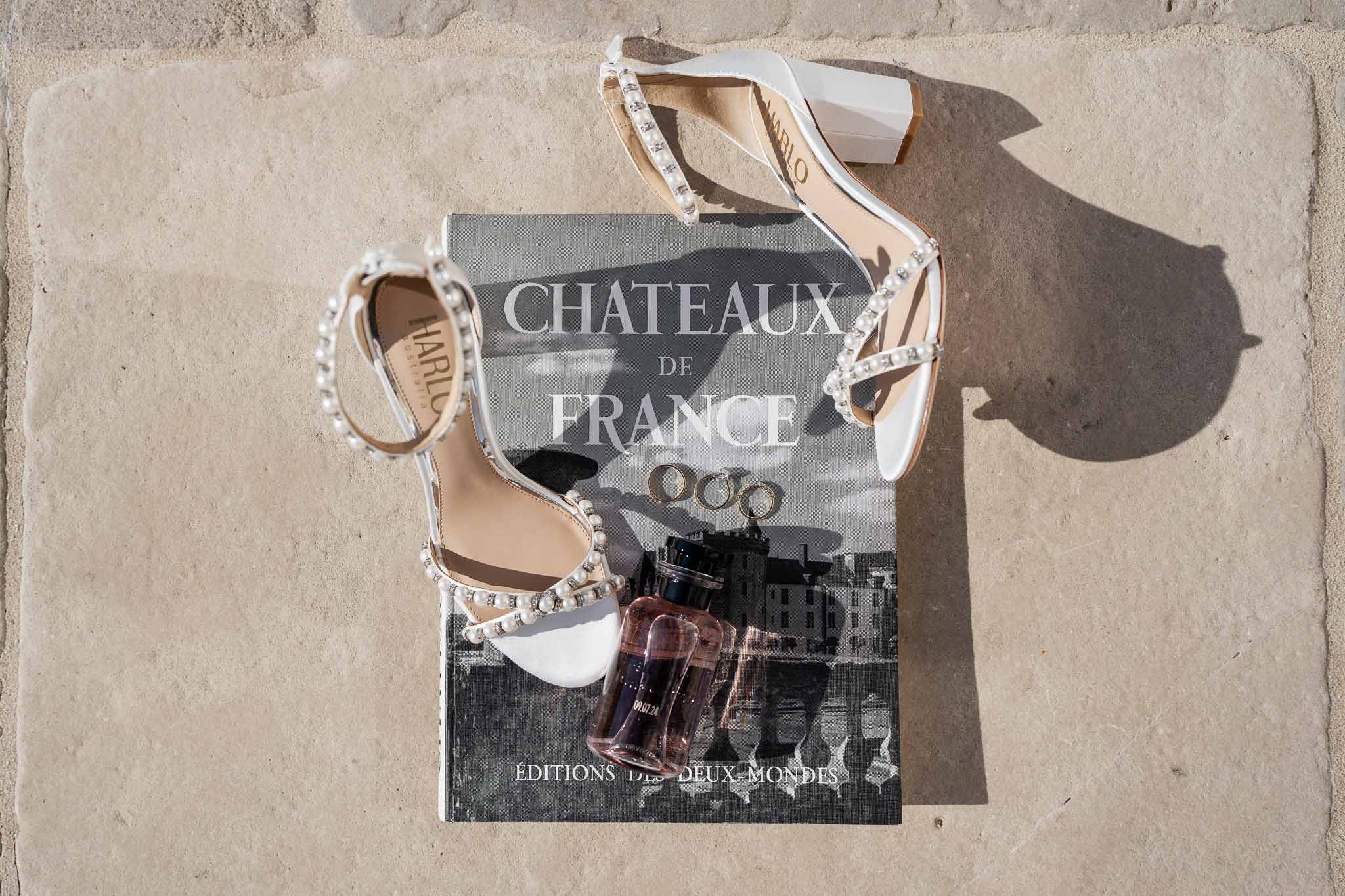 Bridal accessories flat lay with white heeled sandals and wedding ring on stone surface at French château