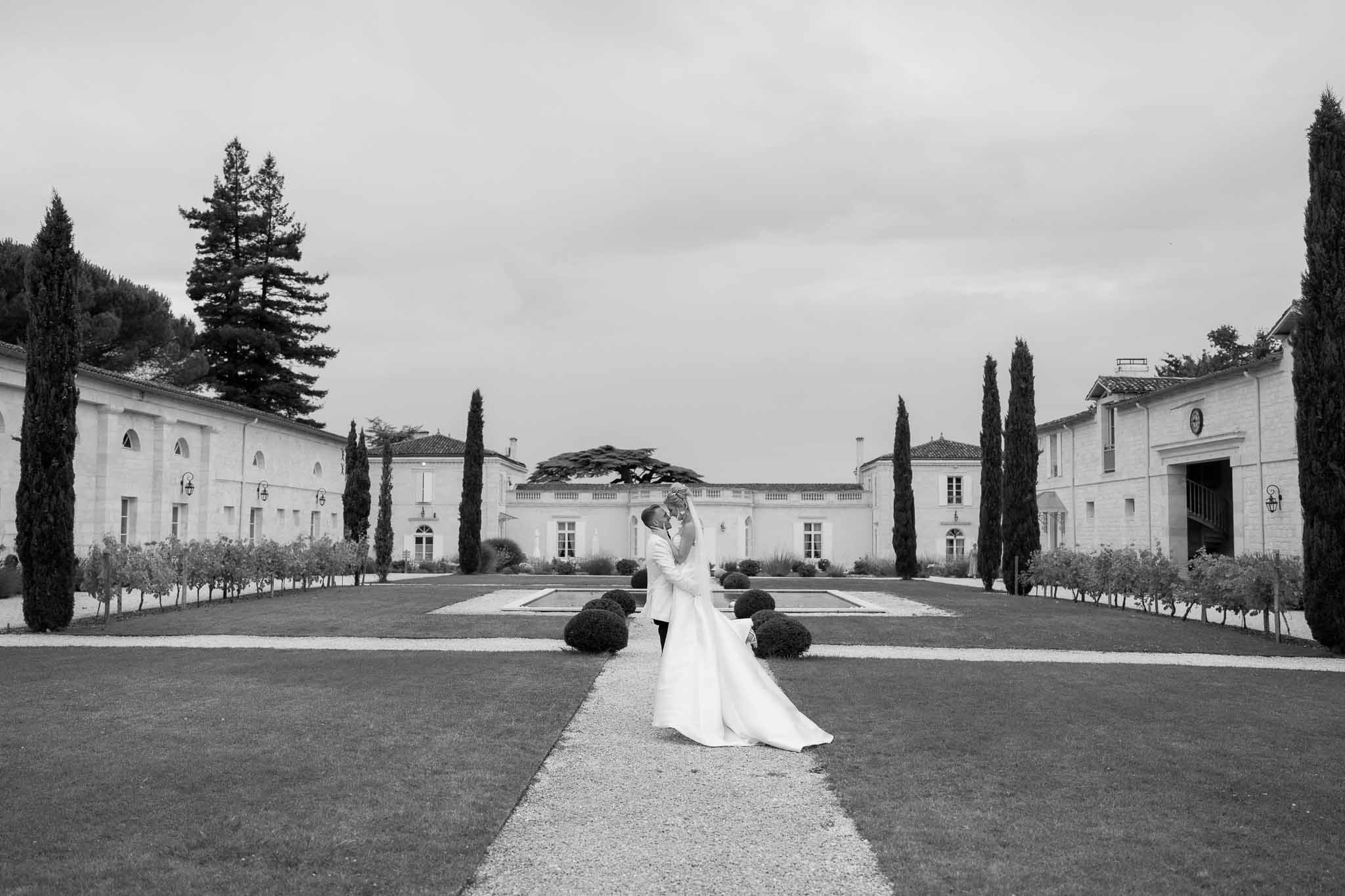 Bride and groom portrait in formal neoclassical estate courtyard with symmetrical hedges and cypress trees
