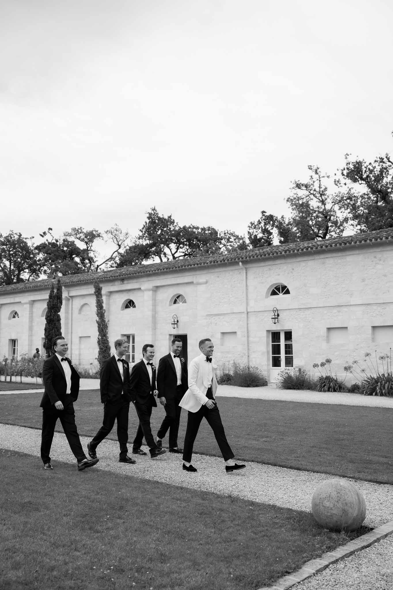 Groom and groomsmen in formal wear walking across courtyard at neoclassical venue