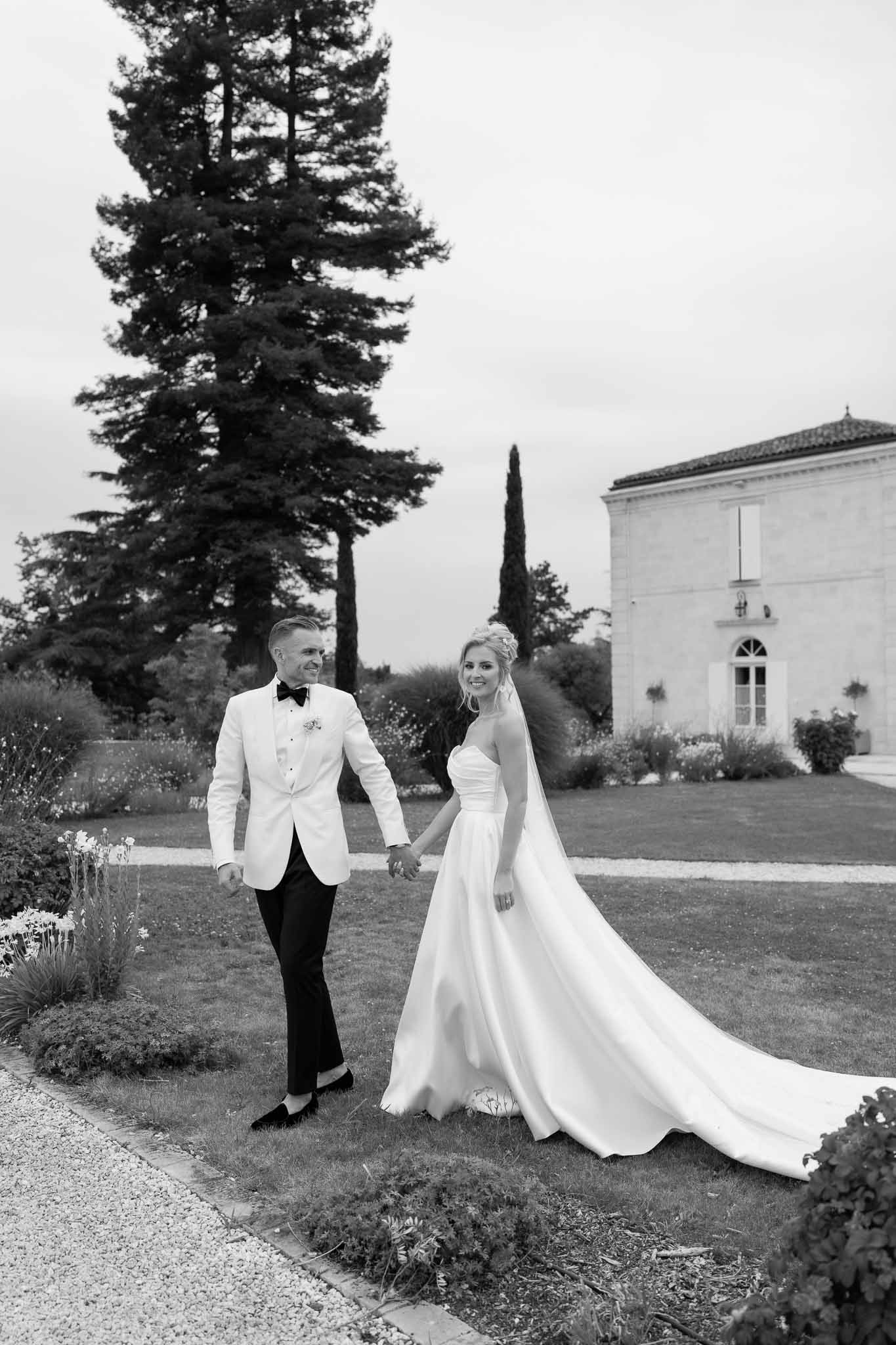 Bride and groom walking hand-in-hand across estate grounds with white chapel in background