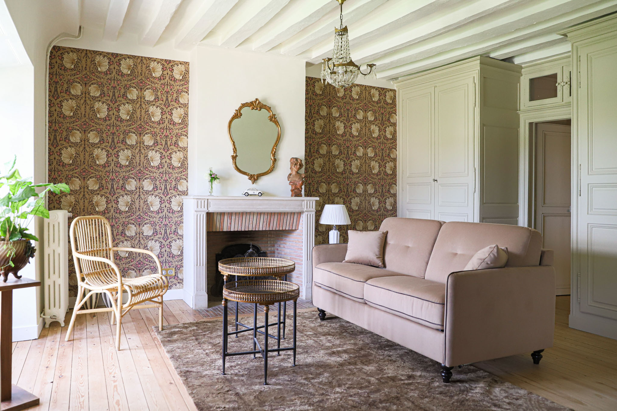 French chateau sitting room with white beams, marble fireplace, patterned wallpaper, and sage green armoires