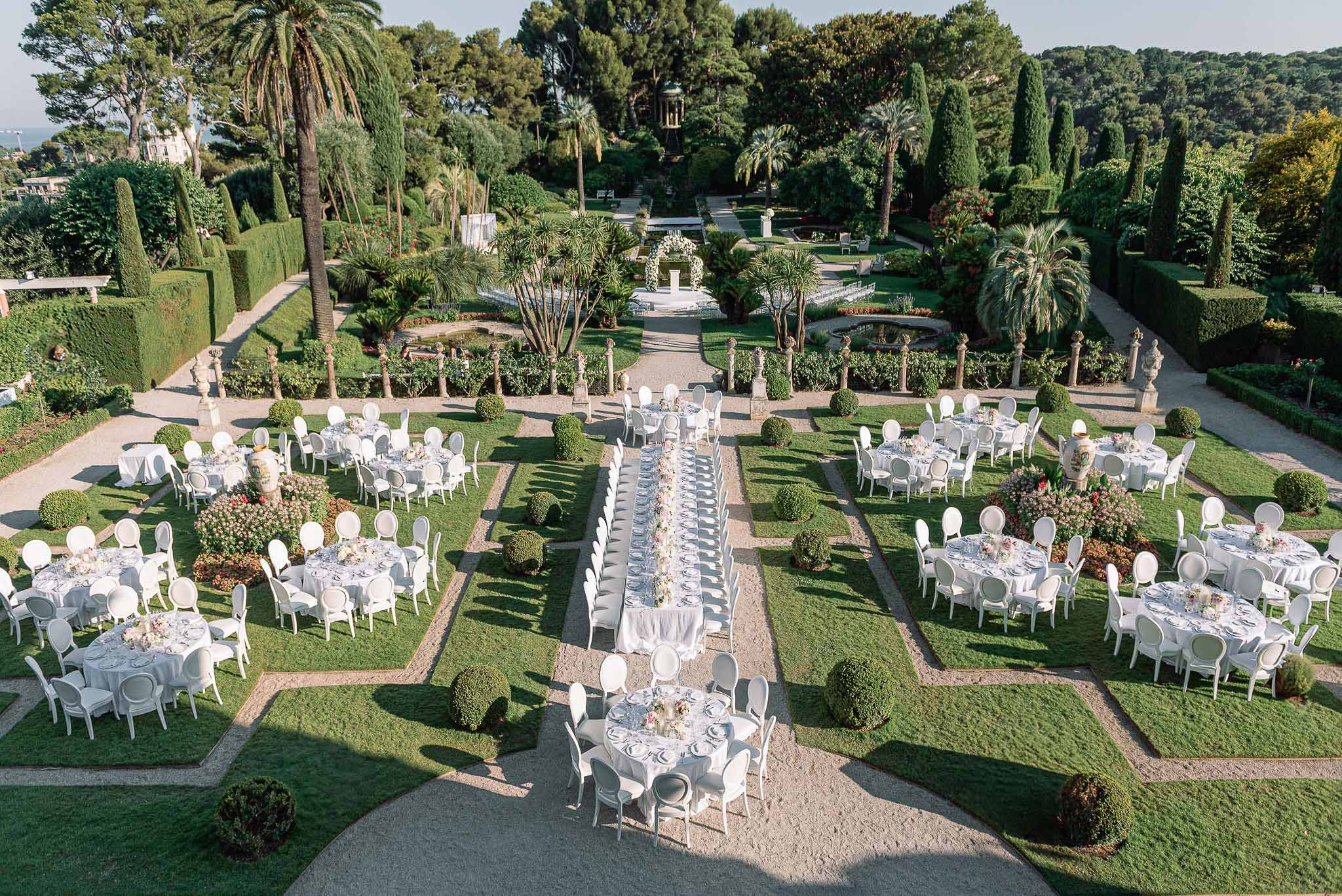 Aerial view of wedding reception setup in formal Mediterranean garden venue with round tables on manicured lawn