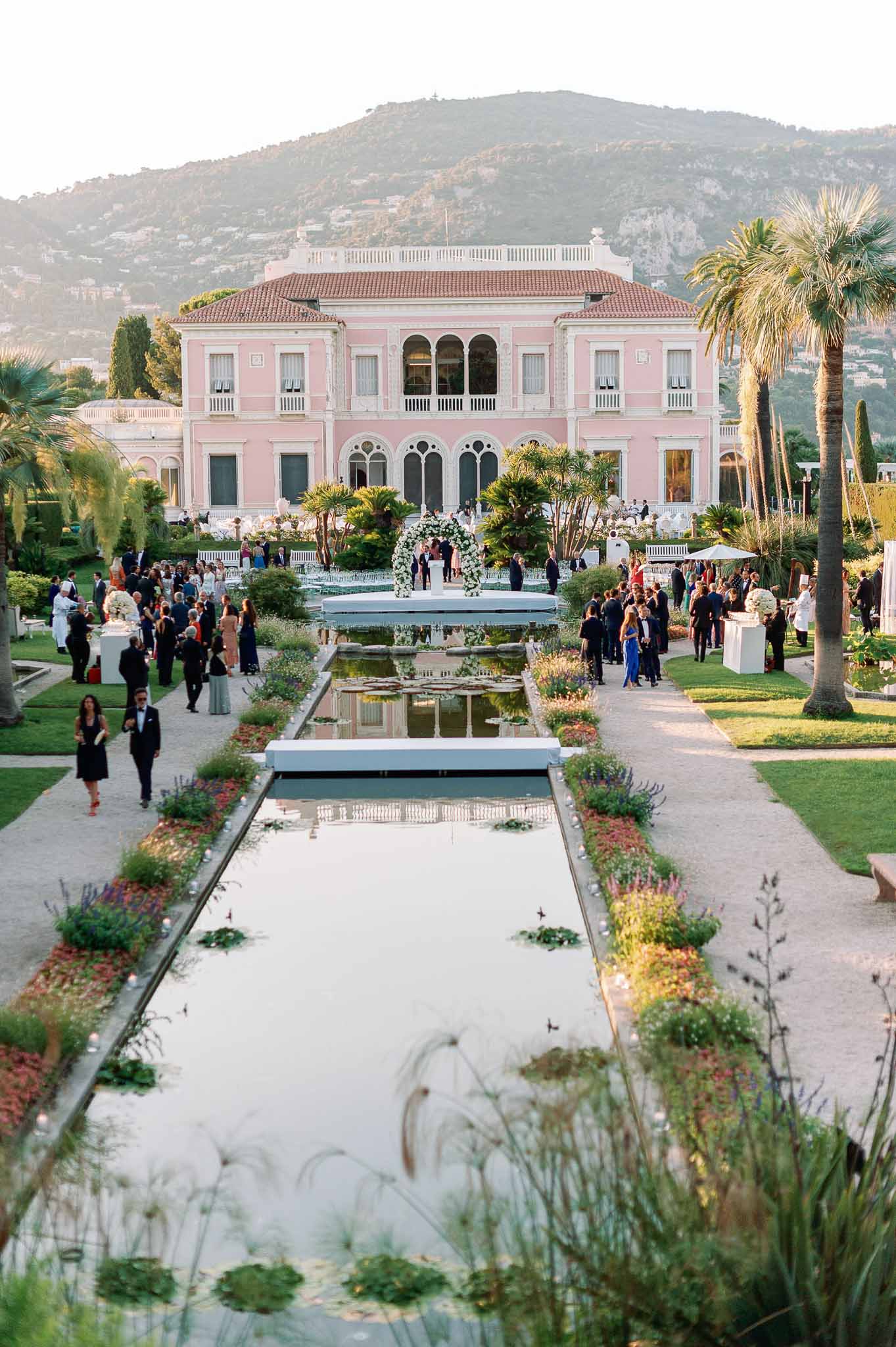 Wedding reception in formal gardens of pink neoclassical villa with guests and reflecting pools